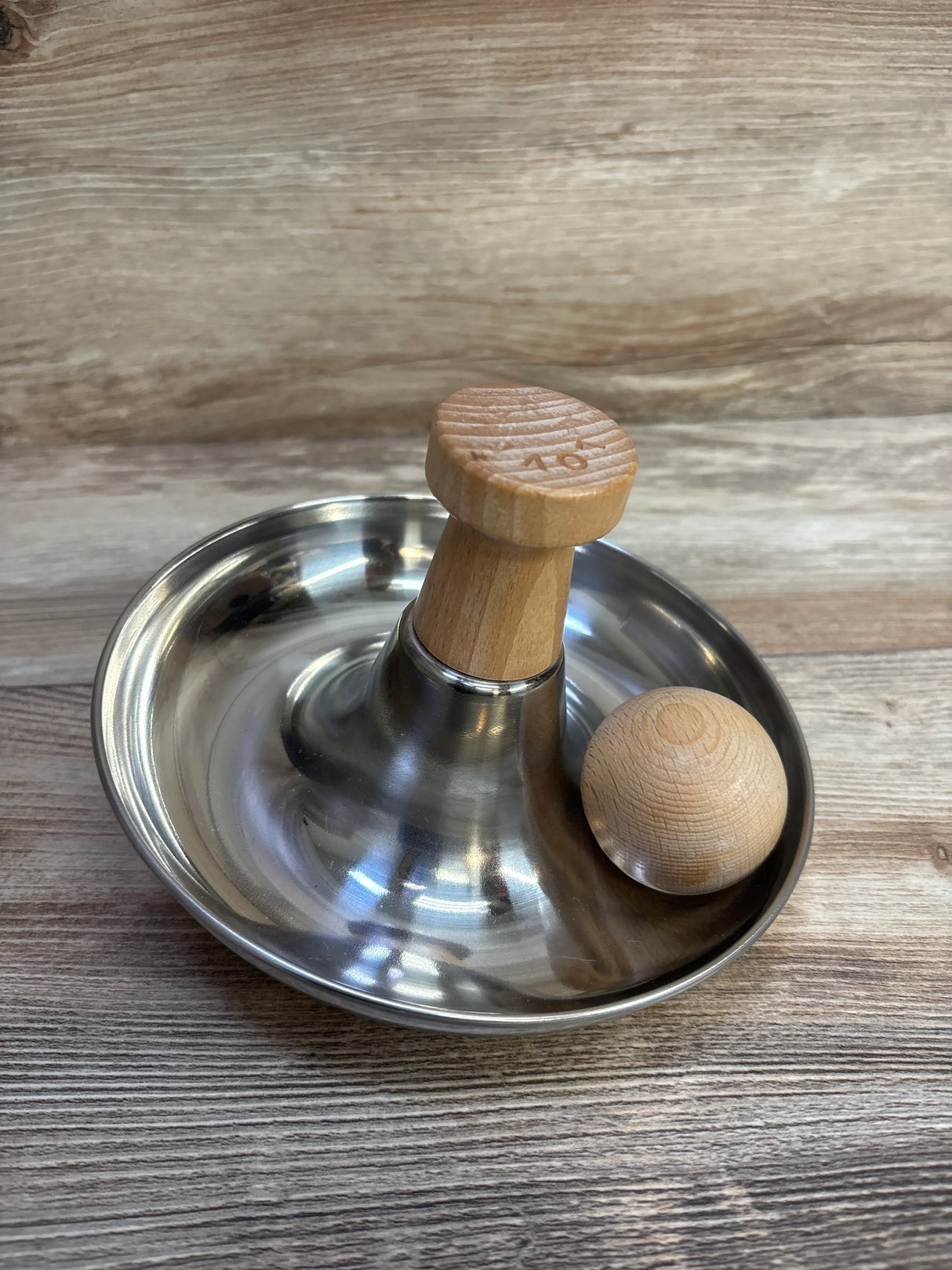Angled view of Lovevery Stainless Steel Tip & Turn showcasing its stainless steel base, wooden handle, and tamper ball on a wood surface