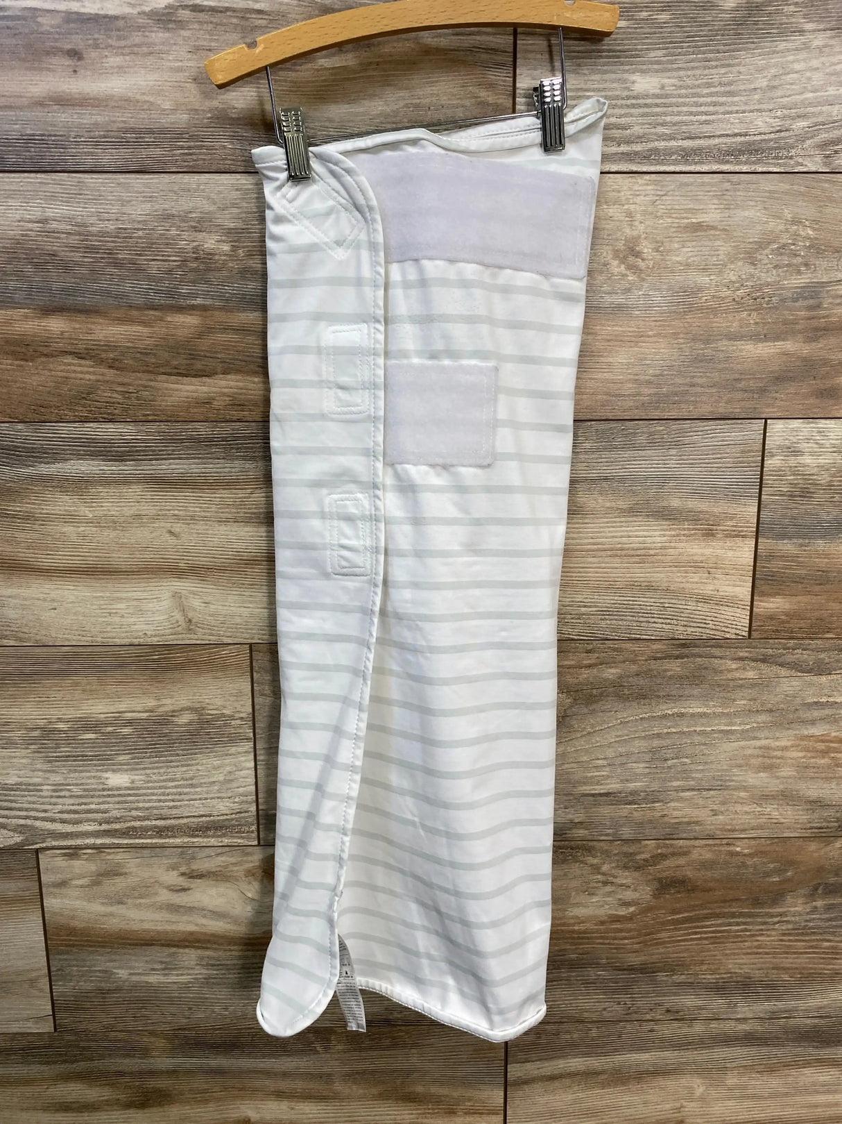White and pale gray striped newborn swaddle hanging on wooden hanger showing Velcro closures and soft inner lining