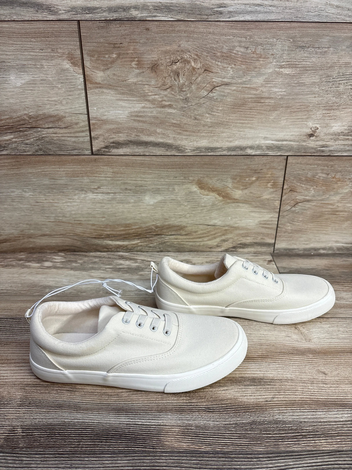 Three-quarter view of Cat & Jack cream canvas kids sneakers (size 5Y) showing low-top lace-up design and white rubber sole on wood floor