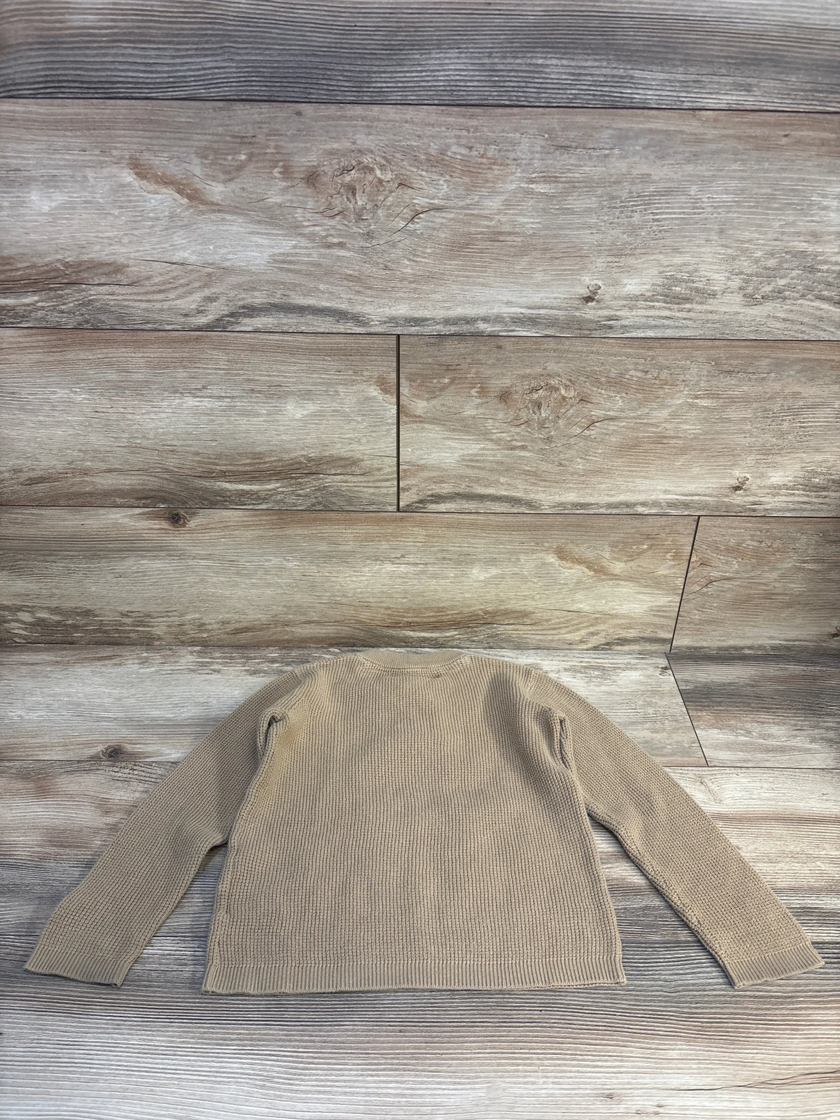 Beige knit long sleeve kids sweater laid flat on wood background