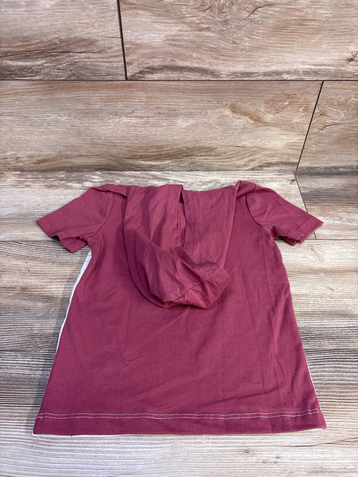 Back view of OshKosh maroon short-sleeve hooded shirt size 5T showing hood and white side stripe on wooden floor background