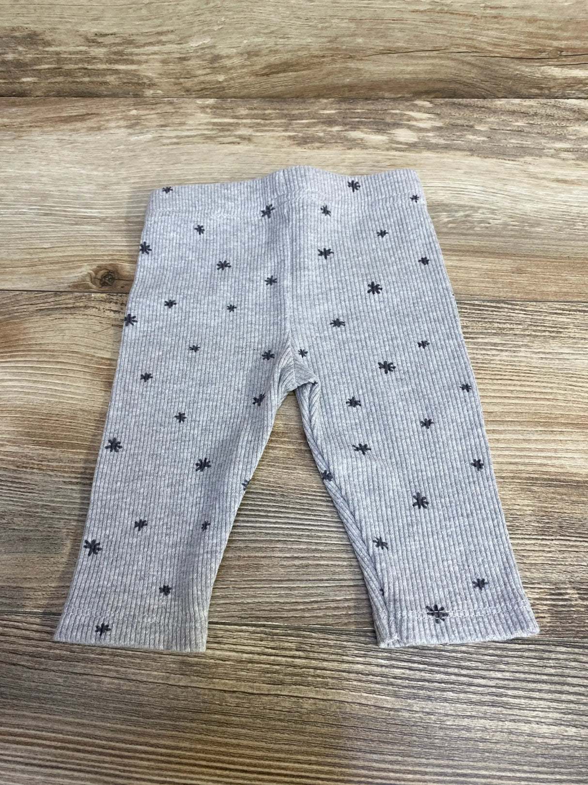 Flat lay of grey ribbed baby leggings (3-6 months) showing front with black star print on wood background