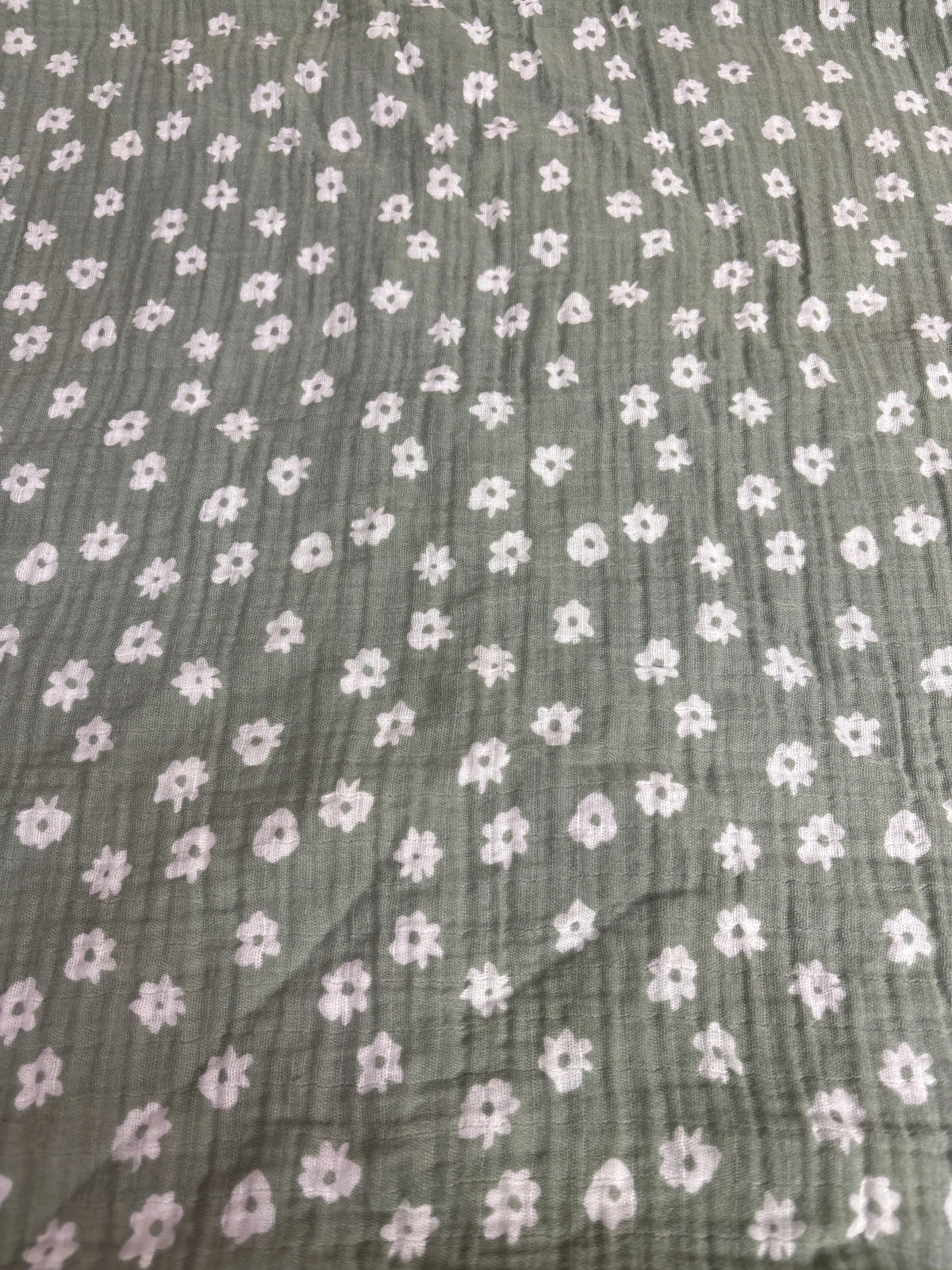 Close-up view of Cloud Island muslin swaddle baby blanket showcasing pale pink flowers on green fabric