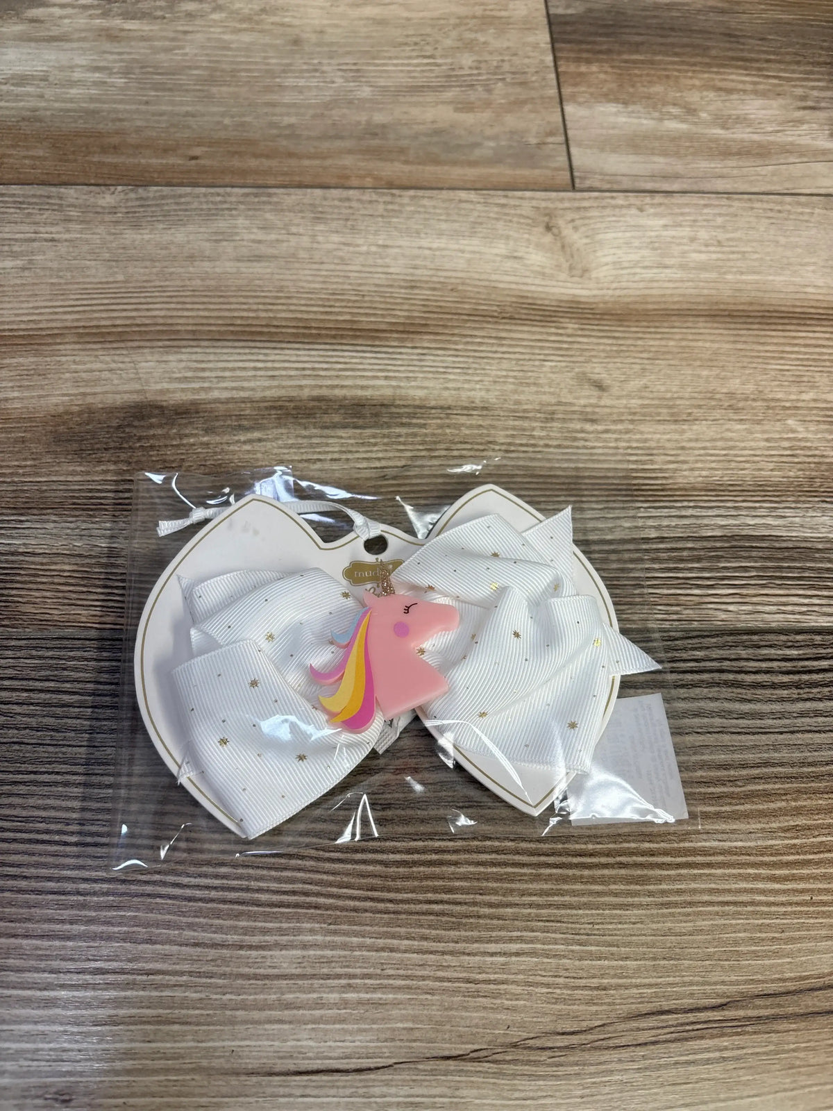 Front view of white unicorn head acrylic hair bow showcasing tiny gold stars in clear packaging on wood surface