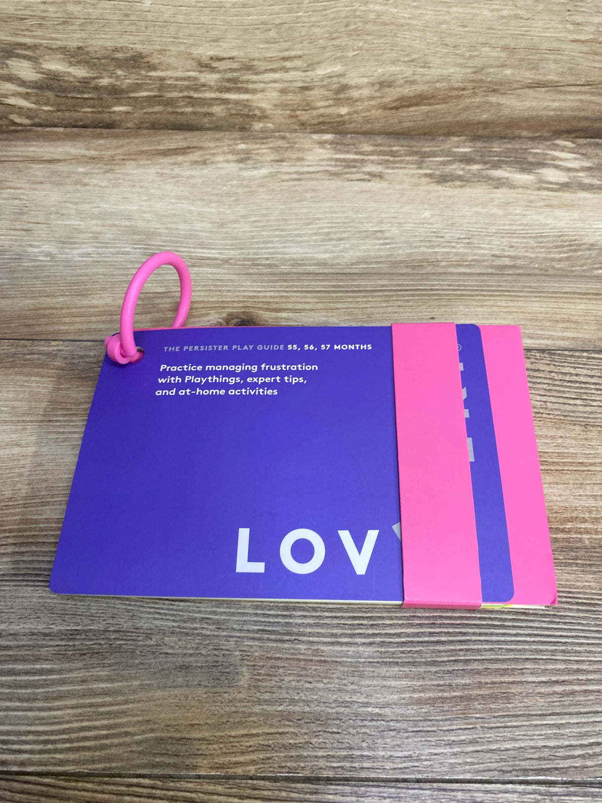 Purple and pink ring-bound play guide for managing frustration in toddlers 55-57 months on wood surface