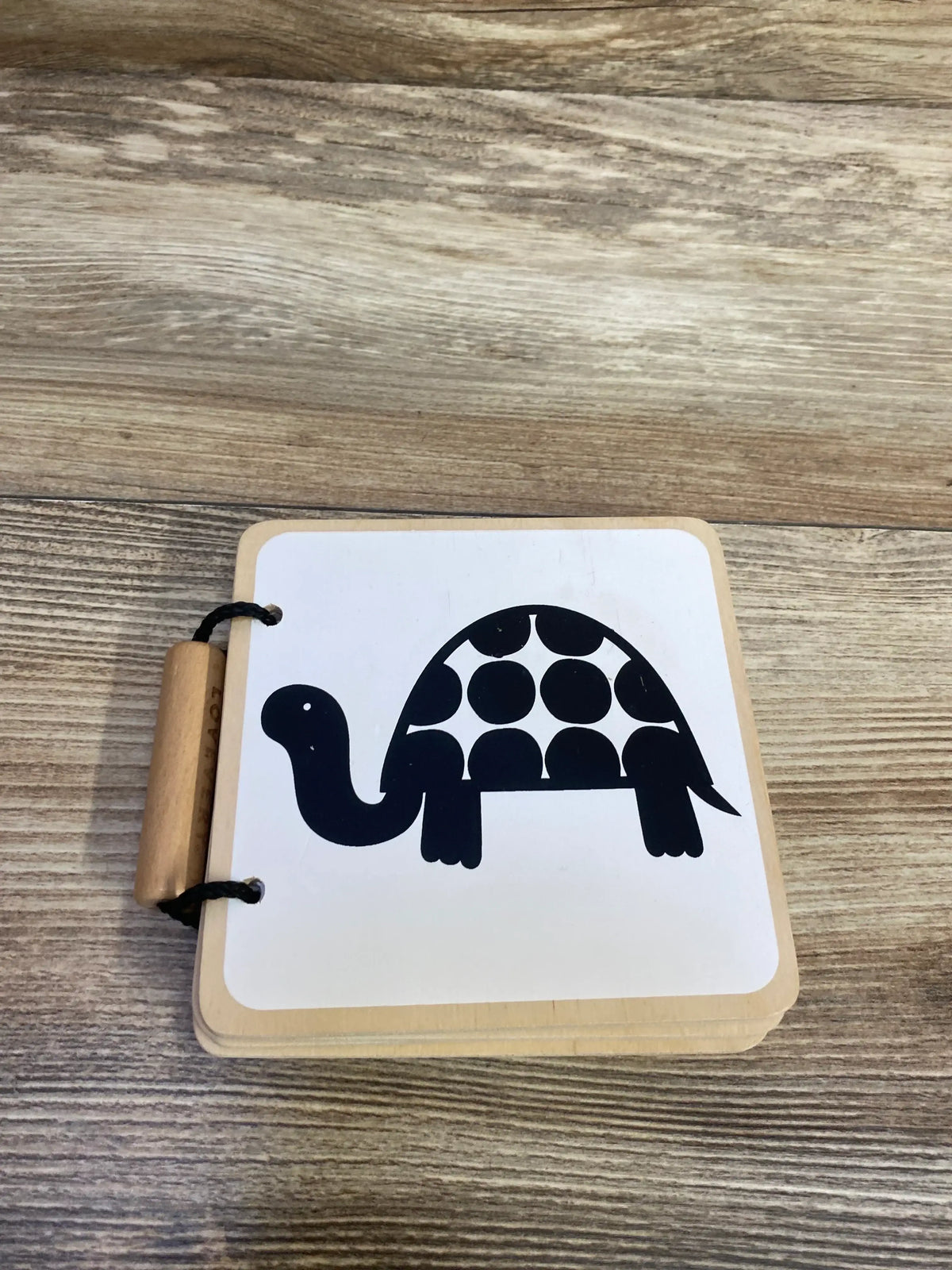 Top view of Lovevery Wooden Book open to black-and-white turtle illustration page bound with metal rings on wood plank background