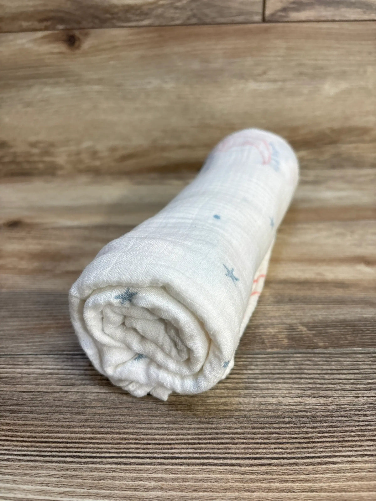 Rolled white muslin baby swaddle blanket with subtle print on wood background