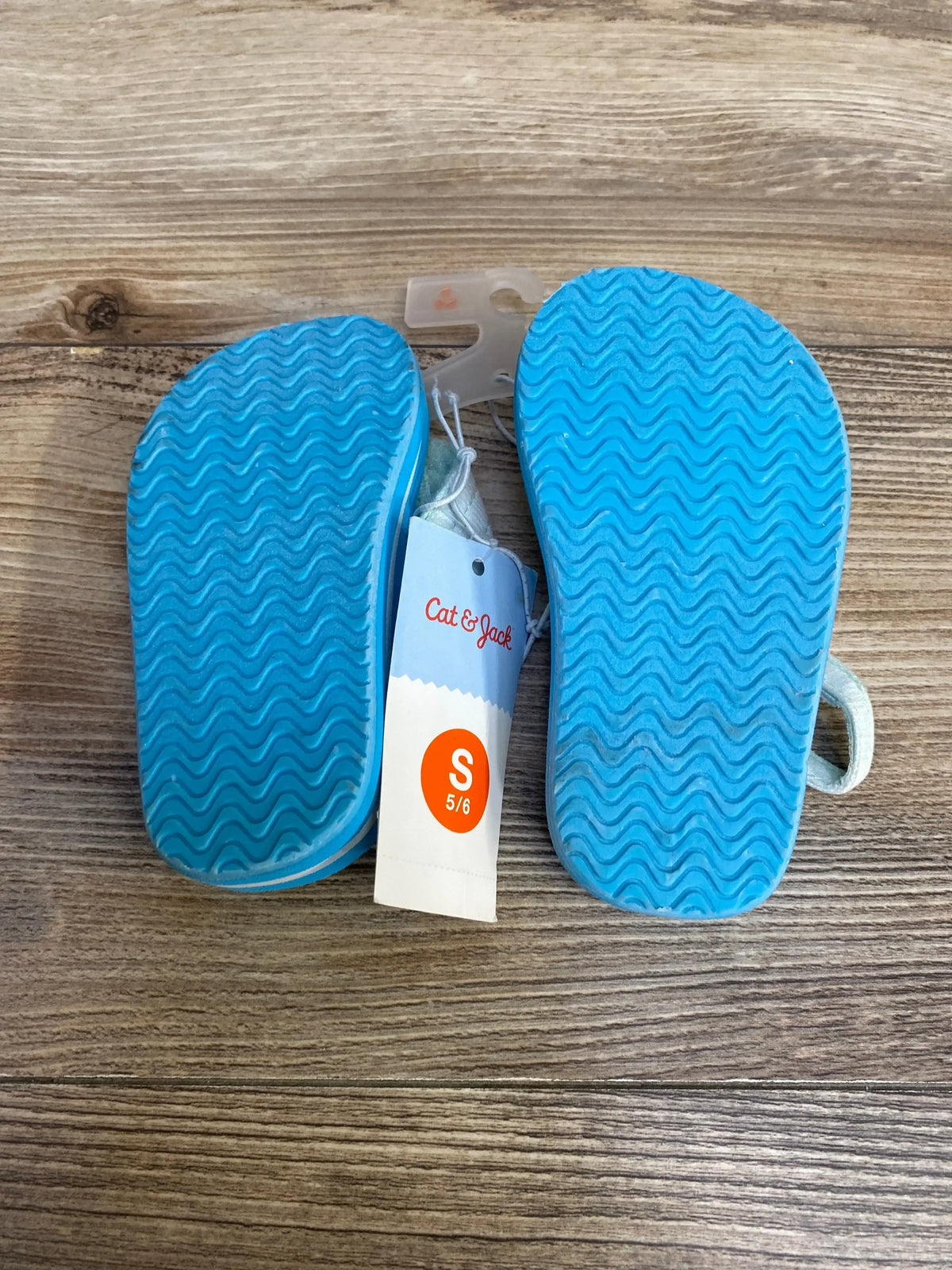 Bottom view of Cat & Jack Shawn toddler sandals showing bright blue wavy soles and visible size tag S 5/6 on wood floor background