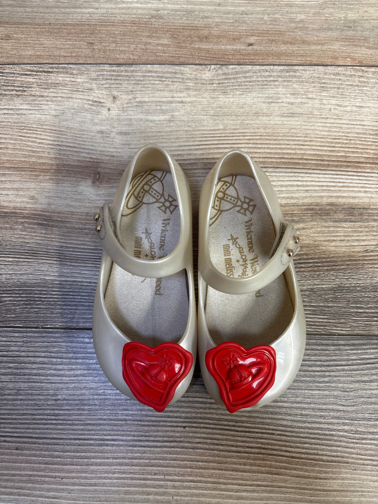 Top-down view of beige Vivienne Westwood x Mini Melissa toddler Mary Jane shoes with red heart orb emblem on wood floor