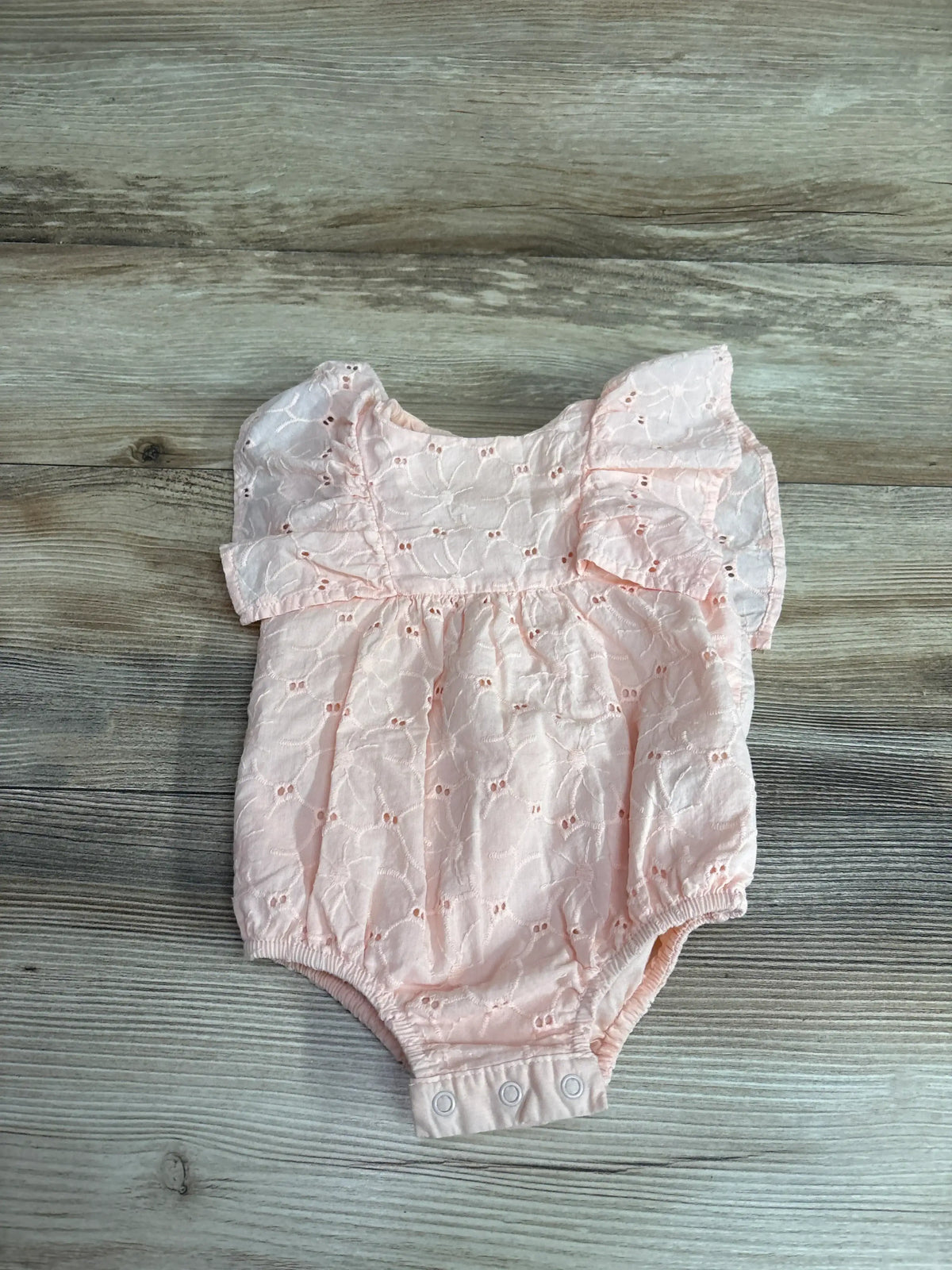 Front view of Cat & Jack blush eyelet bubble romper, size 3 to 6 months, with flutter sleeves and snaps on wood