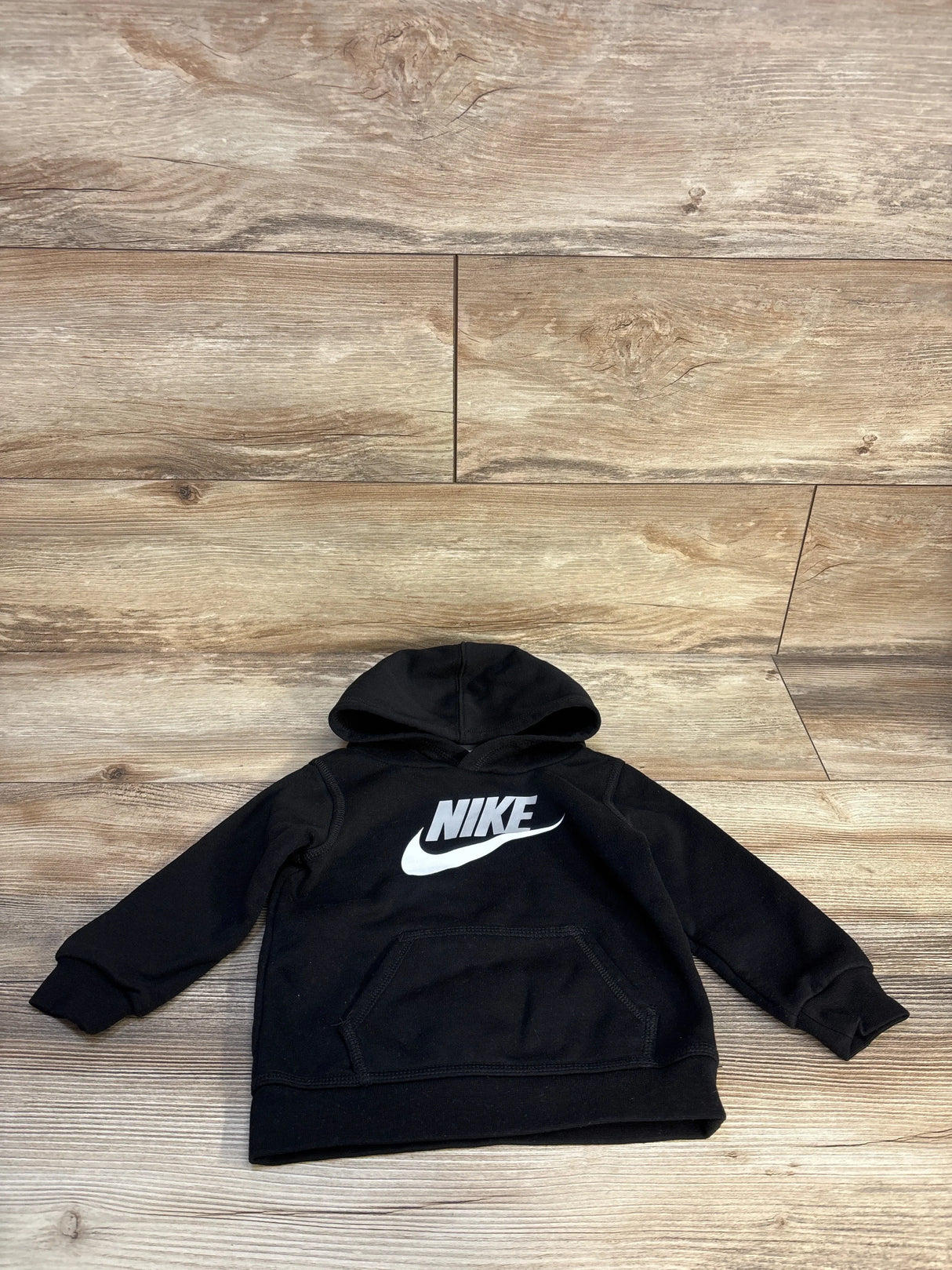 Black kids Nike hoodie with white logo, long sleeves, front pouch pocket on wood background