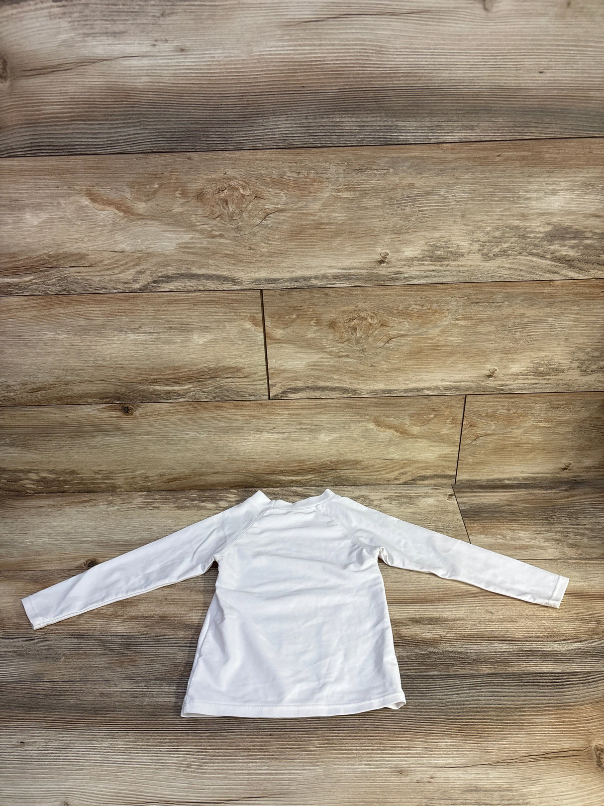 Back view of white long-sleeve UPF 50 toddler rash guard (2T) showcasing raglan sleeves and stitched hem on wood floor background