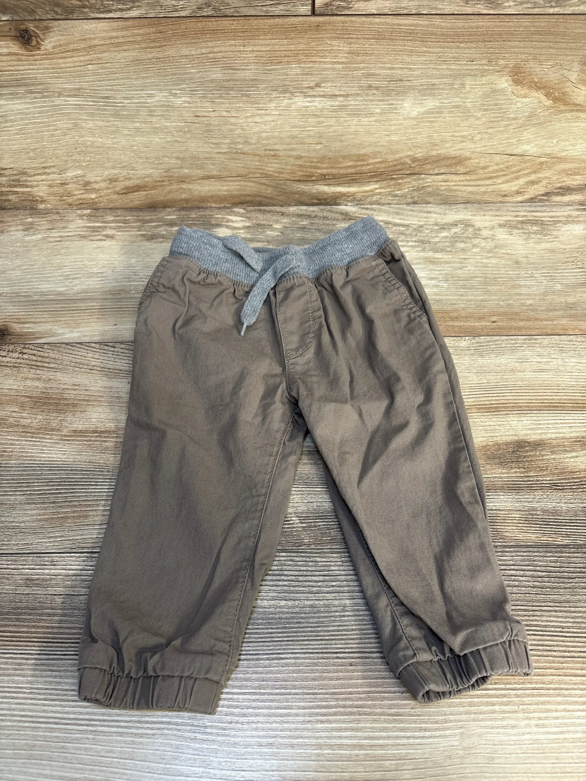 Brown toddler pants with elastic waistband and cuffs on wood background