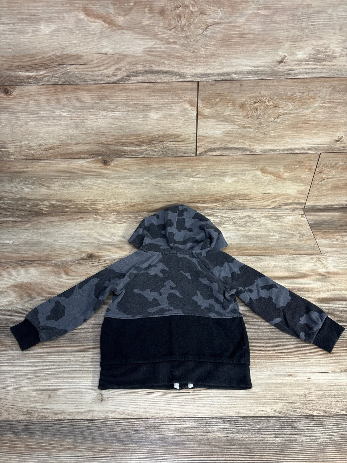 Back view of toddler Under Armour full-zip hoodie showcasing grey and black camo upper with solid black lower on wood floor
