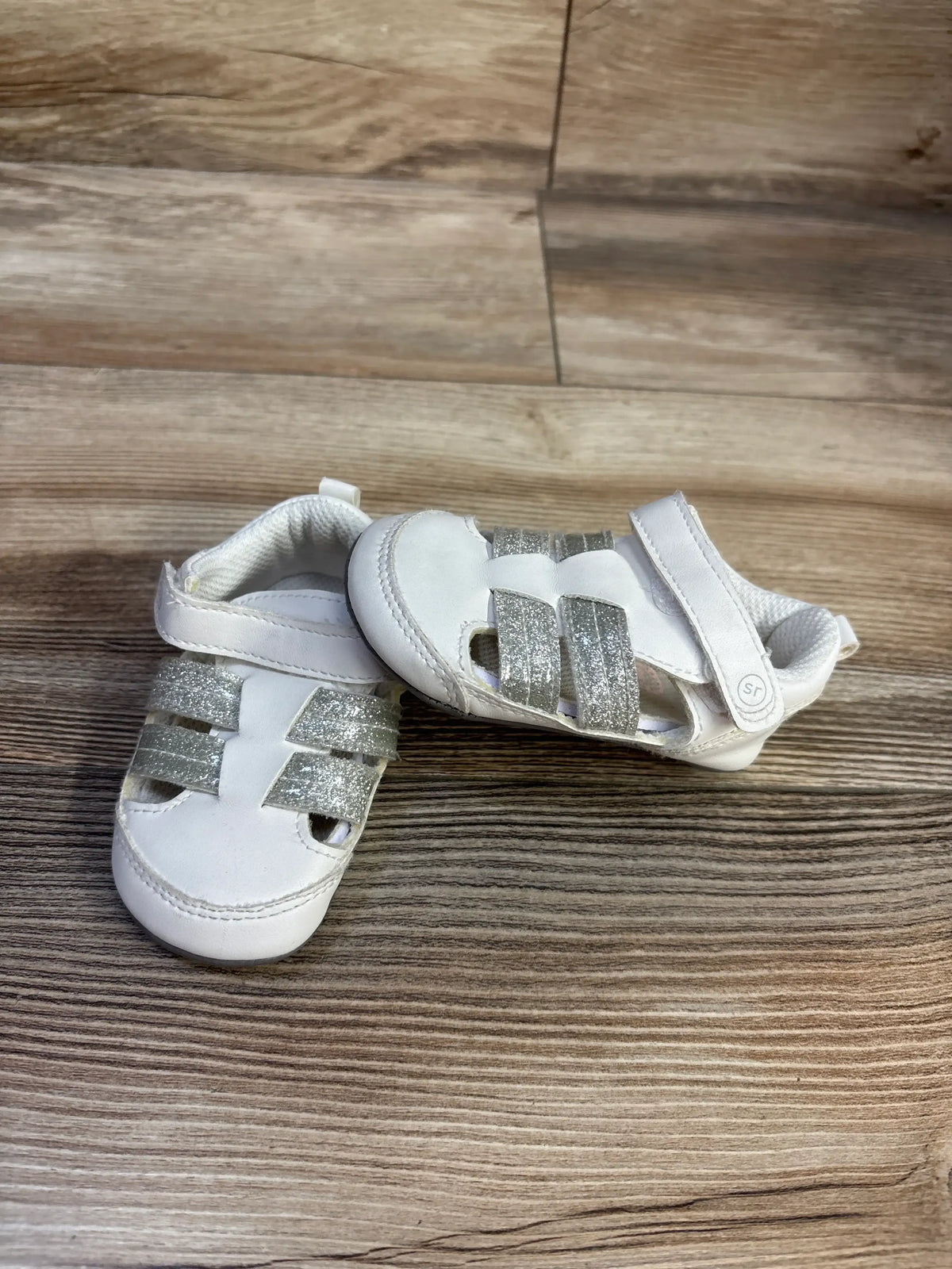 Top view of Surprize by Stride Rite fisherman sandals showcasing glittery silver straps on wood grain