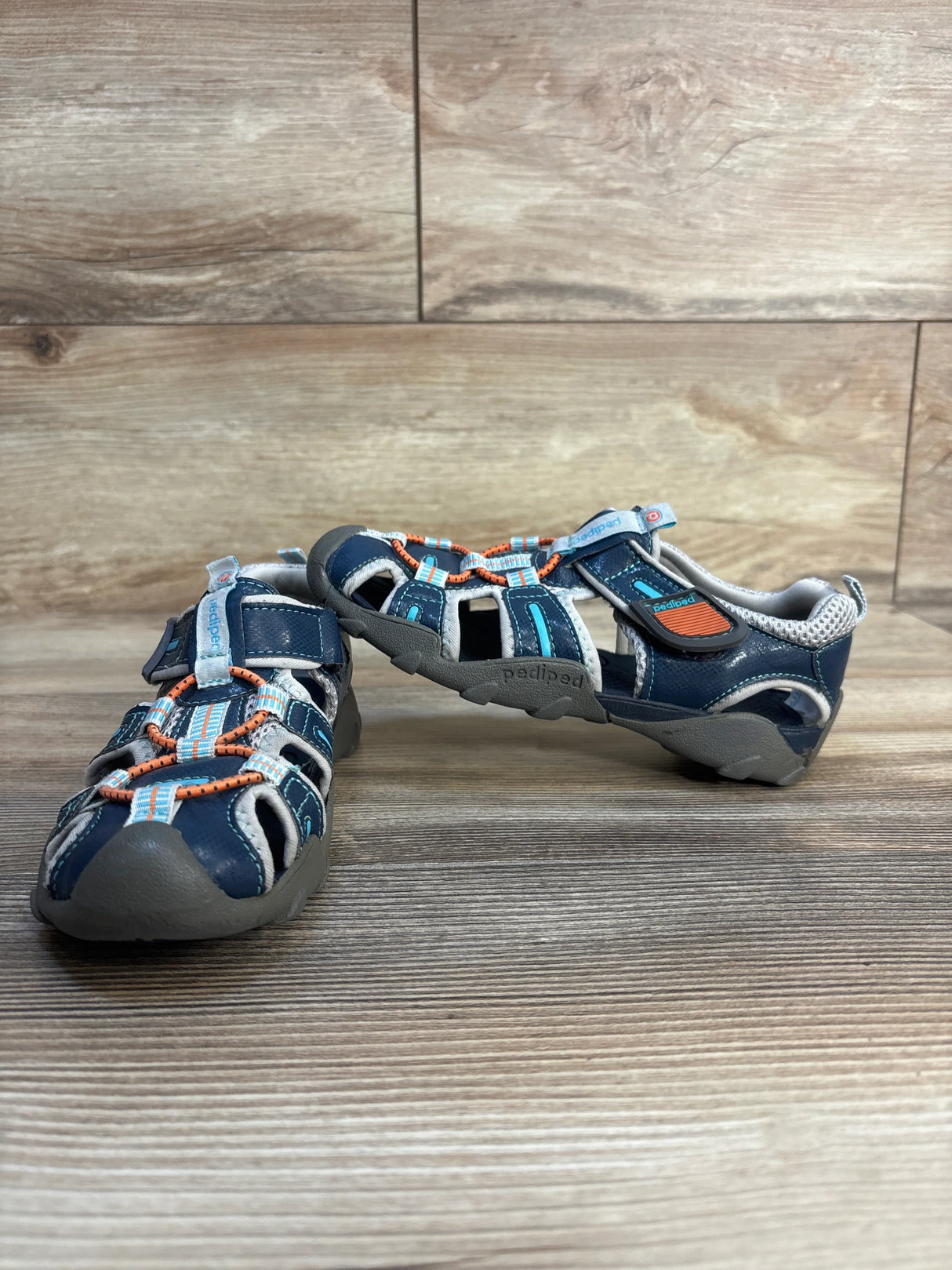 Front three-quarter view of Pediped Flex Canyon water sandals (size 11.5C) showing closed-toe bumper, elastic bungee lacing and velcro strap on wooden floor