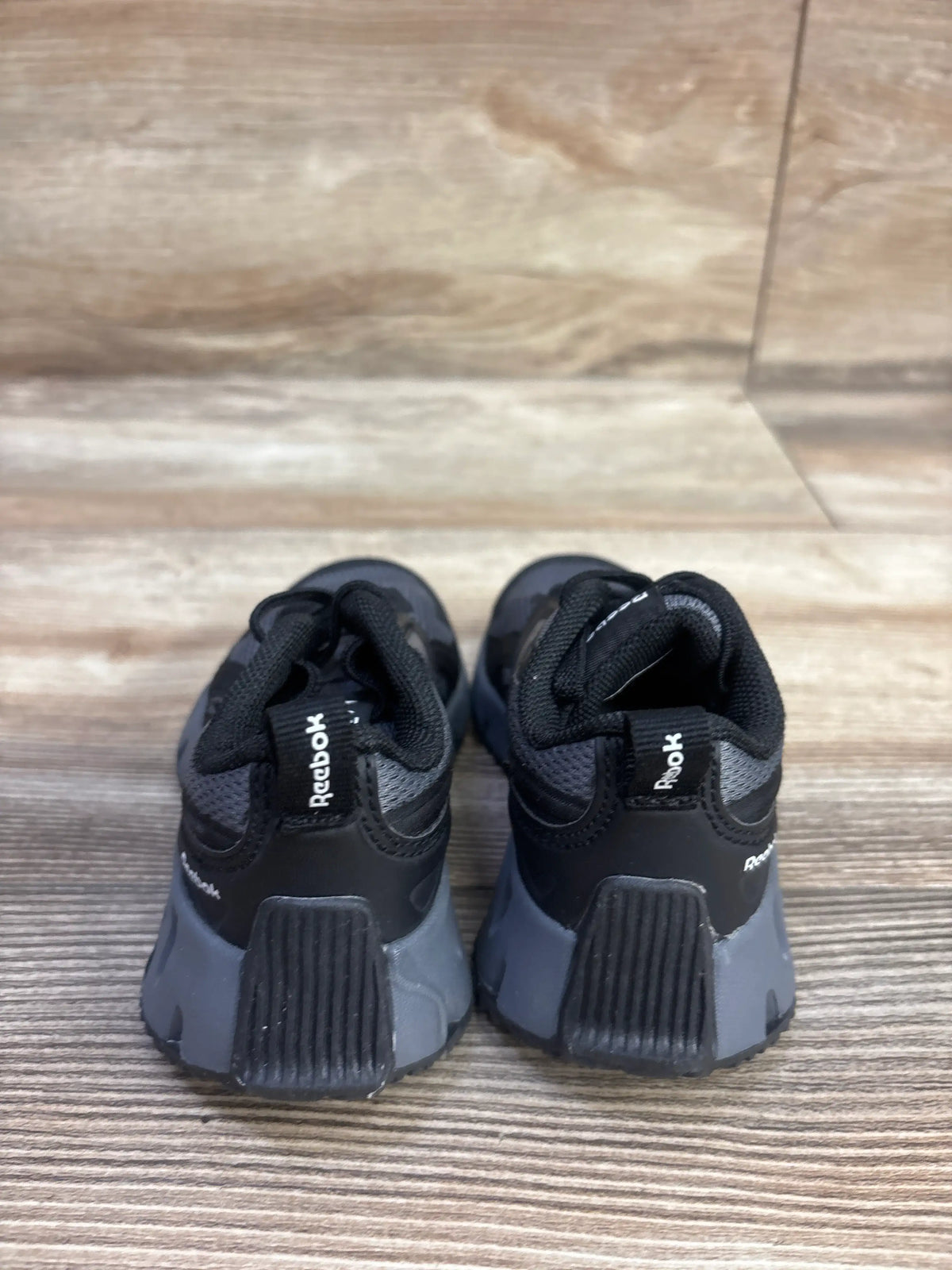 Rear view of Reebok Charge Run sneakers in black, size 6C, showcasing textured heel panels on a wood-grain floor