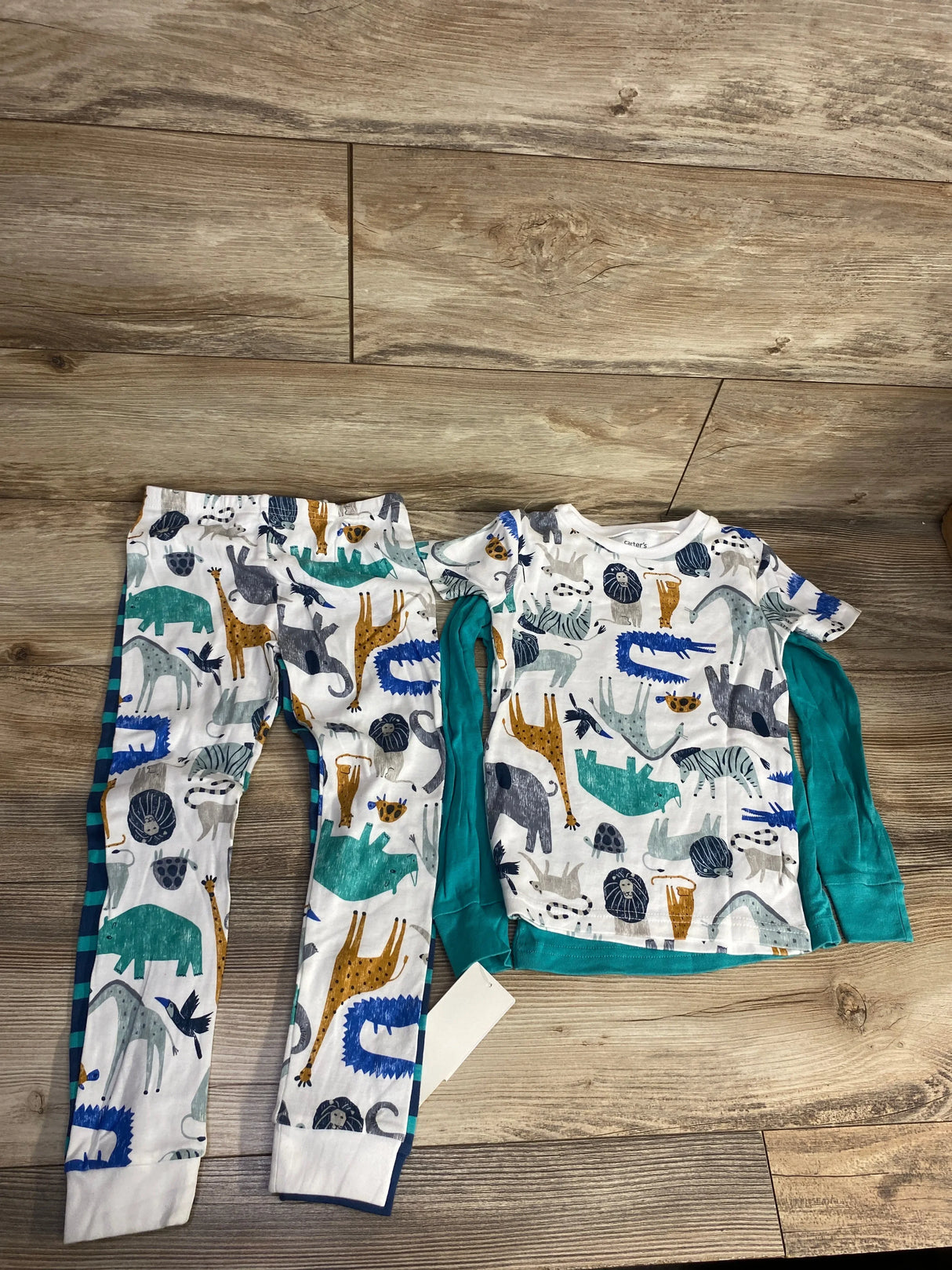 Flat lay of 4-piece sleep set (size 5T): animal-print short-sleeve top, teal long-sleeve, two matching pants on wood floor