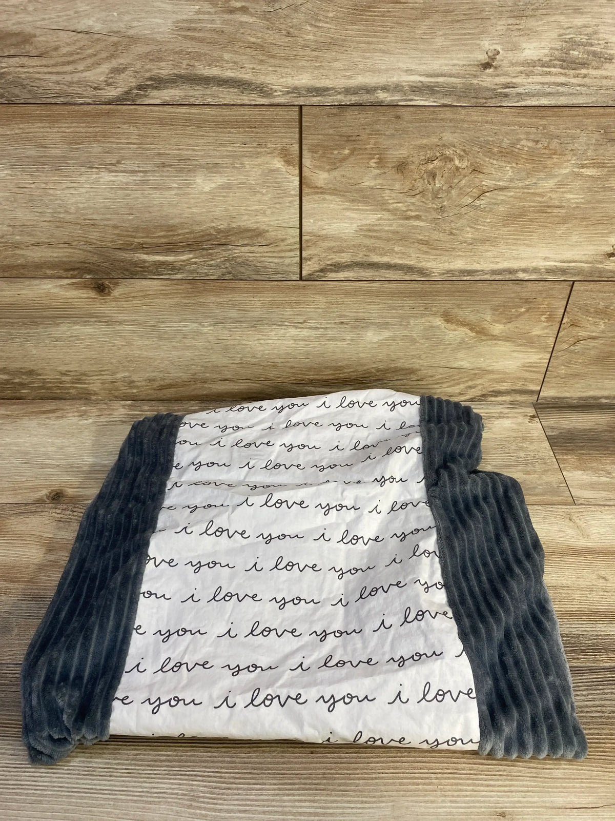 Top-down view of Cloud Island changing pad cover showing ‘i love you’ script on white center and gray ribbed sides on wood