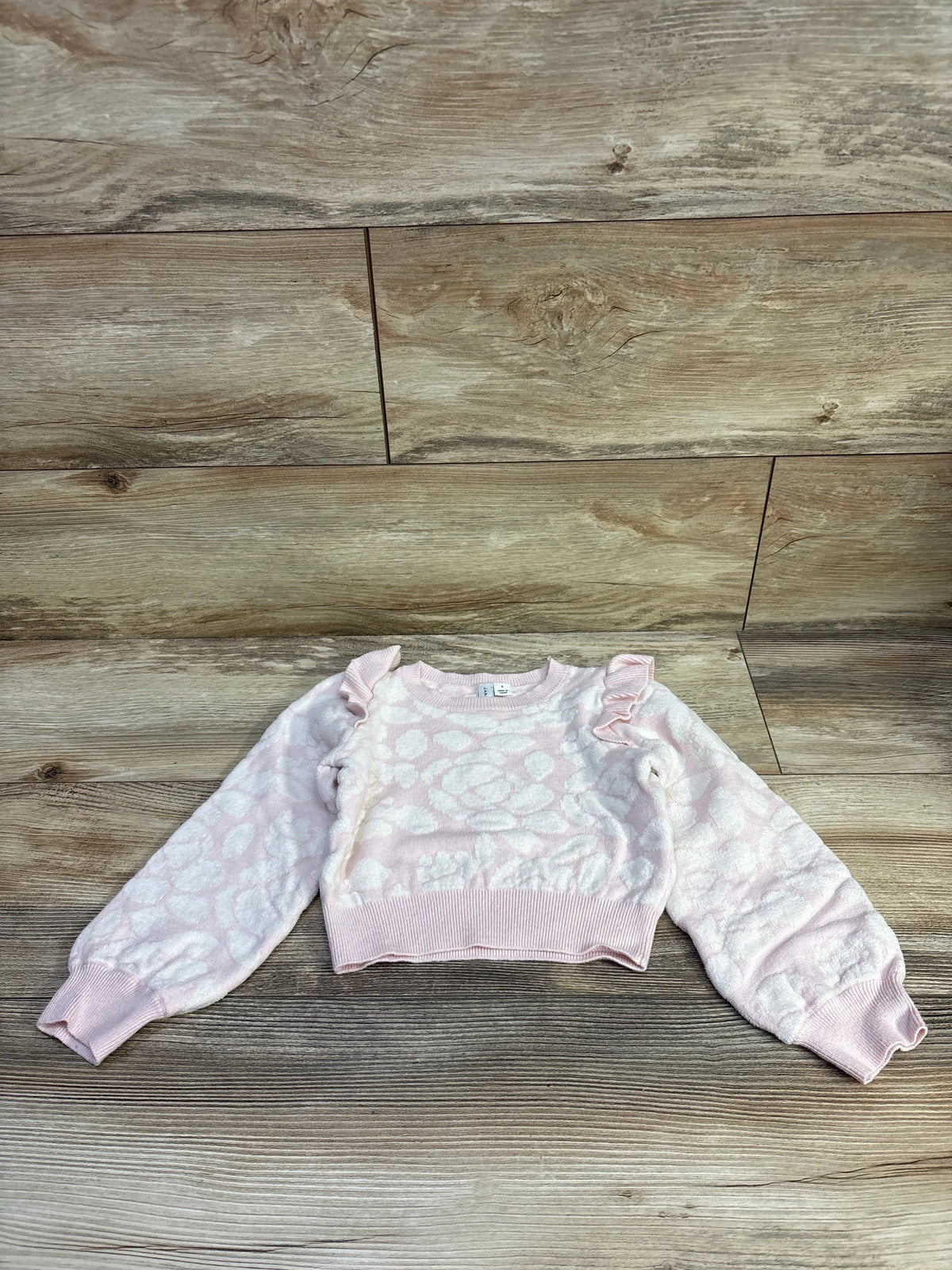 Flat lay of pink toddler sweater size 4T with raised floral pattern, ruffle shoulders and ribbed cuffs on wood background