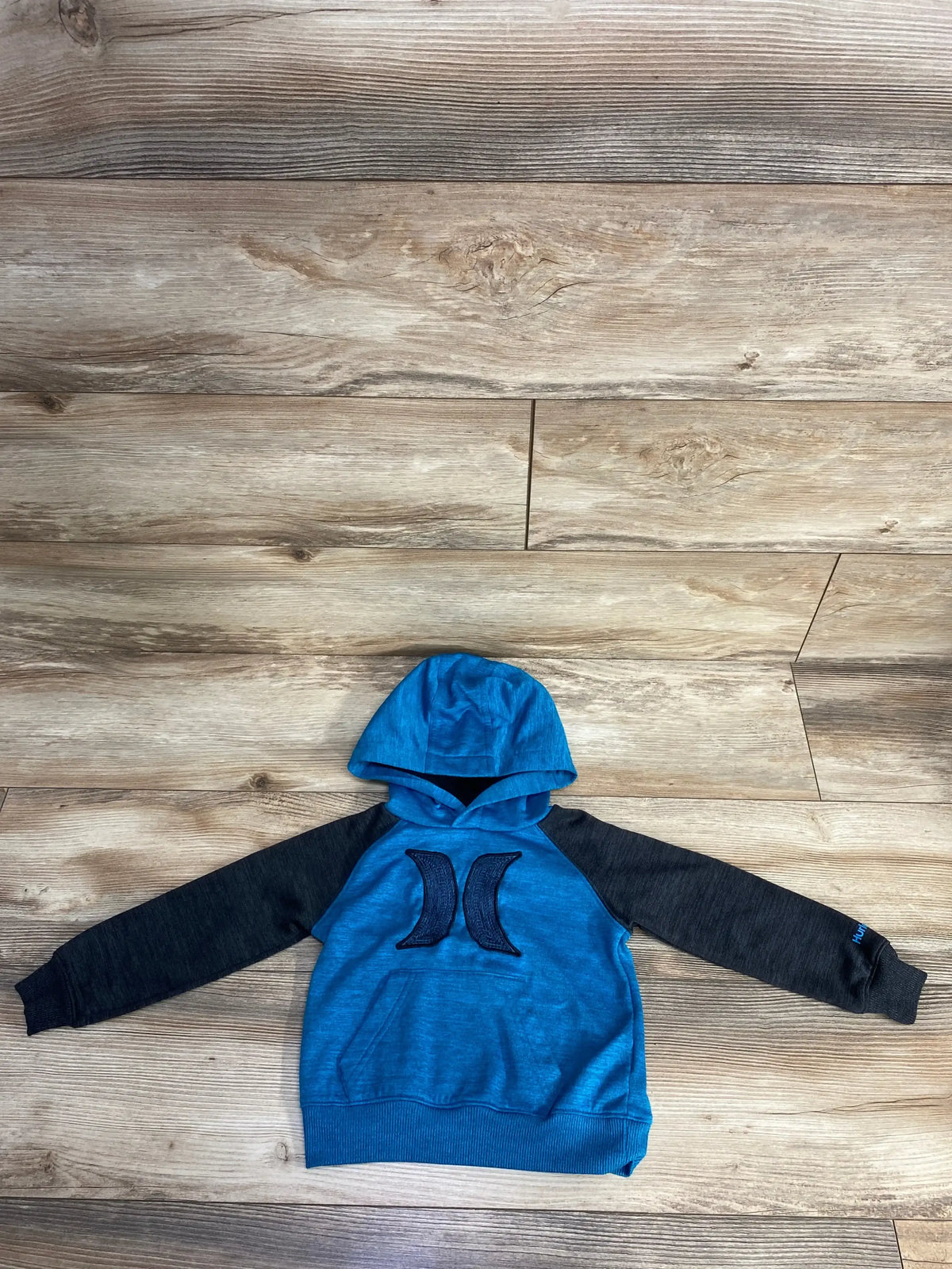 Blue and black Hurley hoodie for kids laid flat on wooden floor with logo on chest and sleeve