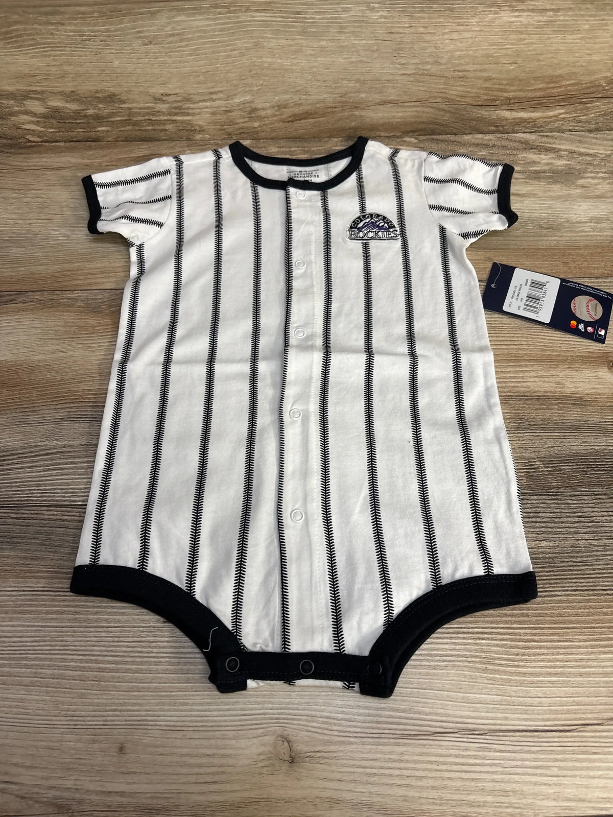 Flat lay of white Colorado Rockies pinstripe romper showing front snaps, black trim, and team patch on wood background