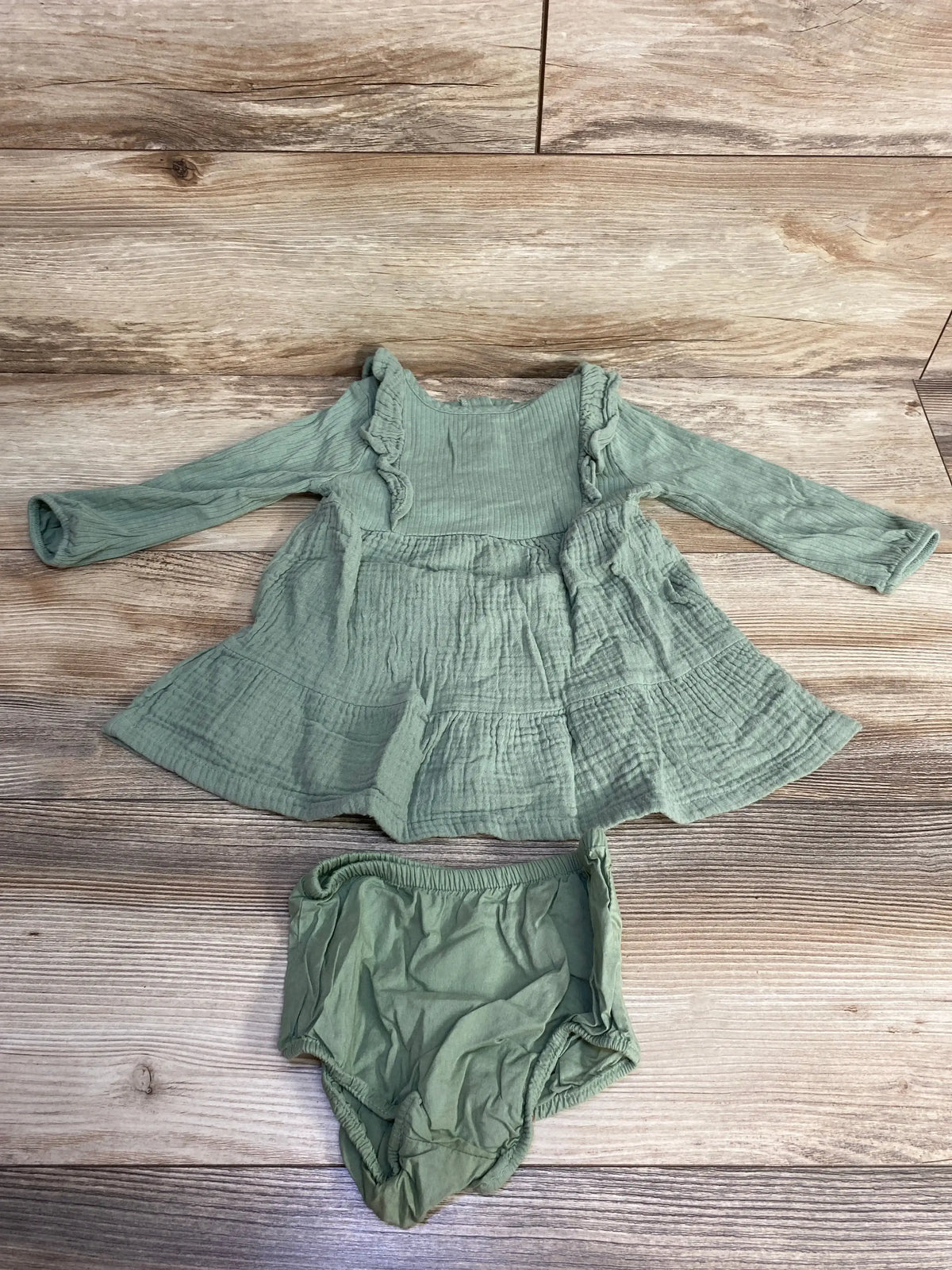Sage green baby dress and bloomers set on wood background, long sleeve cotton outfit