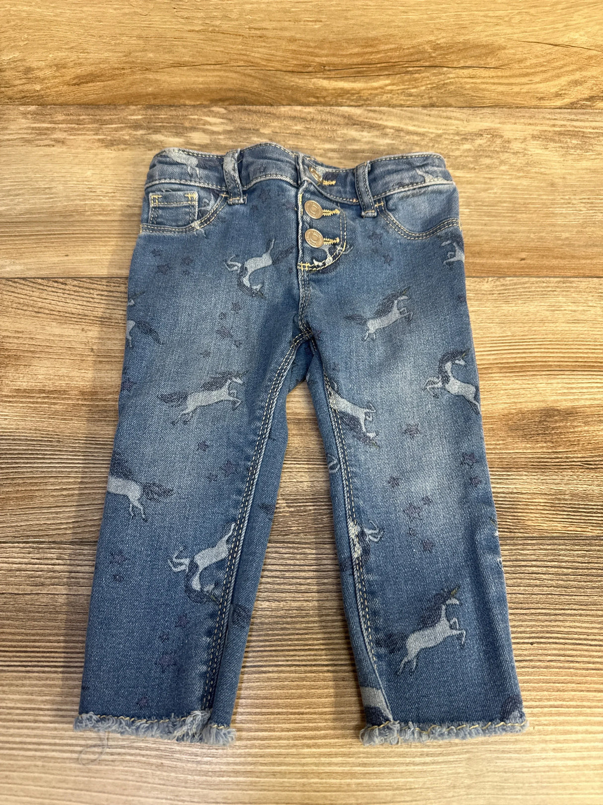 Toddler blue unicorn print jeans with frayed hems on wood background