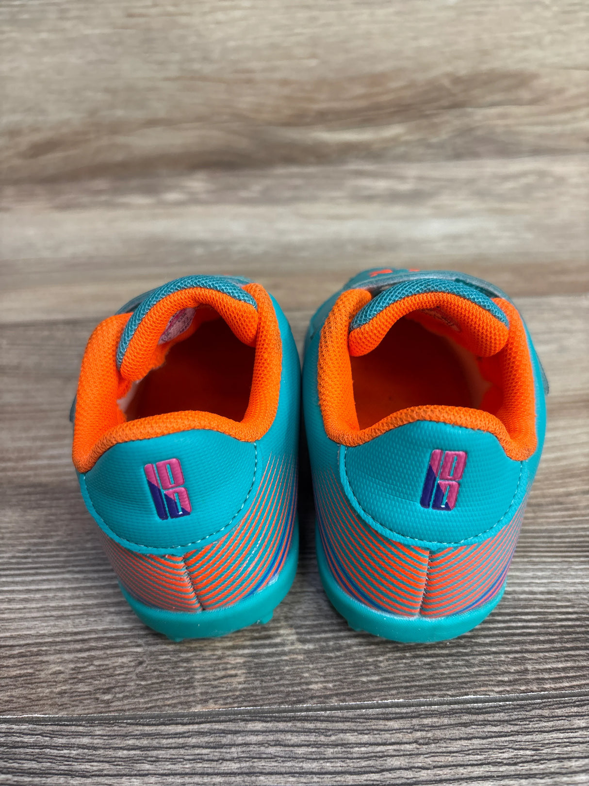 Back view of toddler sports shoes in turquoise with orange lining and pink and blue logo on wooden floor