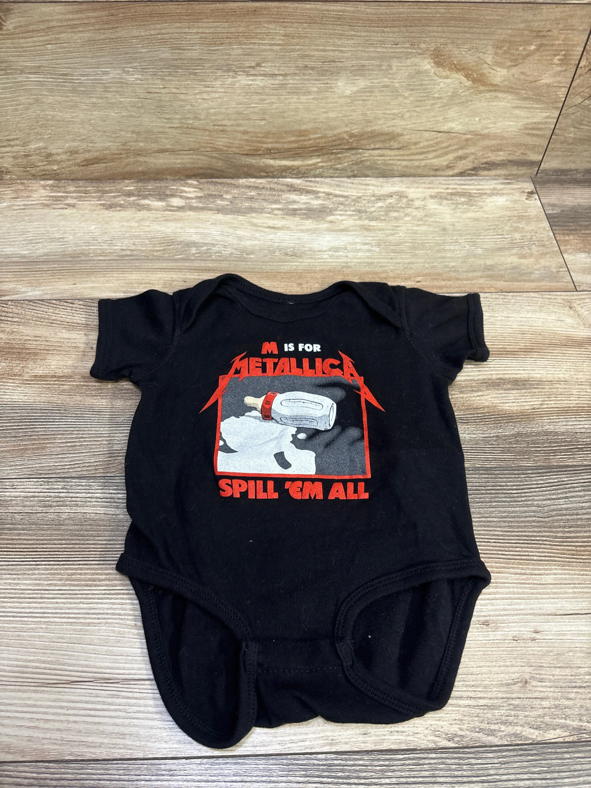Front view of black baby bodysuit with red and gray M Is for Metallica Spill Em All graphic on wood floor