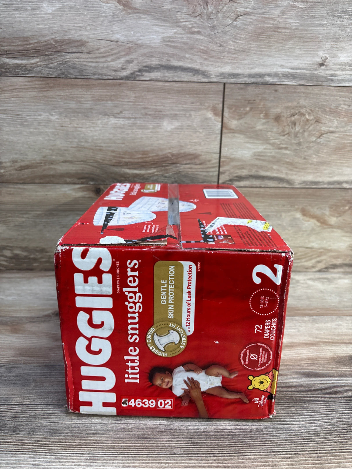 Huggies Little Snugglers size 2 diaper box on wood floor, red packaging, 72 count.