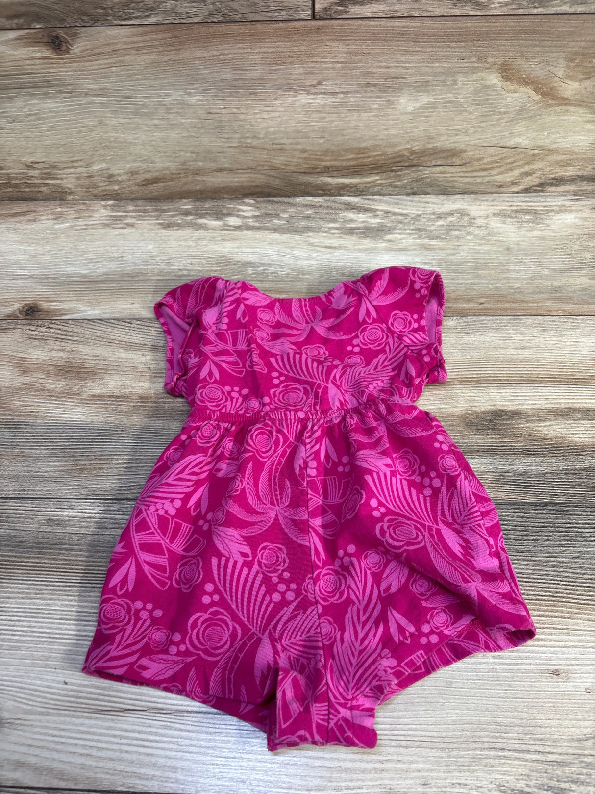 Top-down view of Baby Gap pink floral shortie romper size 6-12 months showcasing gathered waist and cap sleeves with light wood background