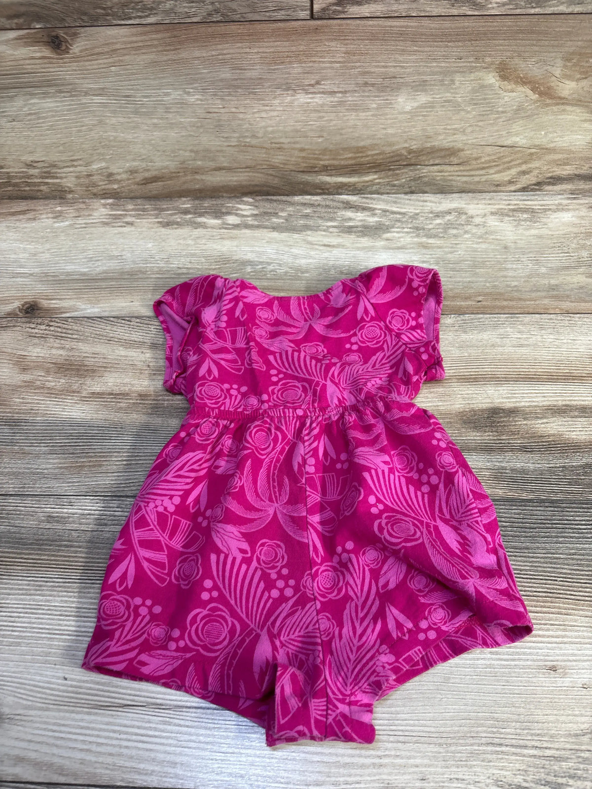 Top-down view of Baby Gap pink floral shortie romper size 6-12 months showcasing gathered waist and cap sleeves with light wood background