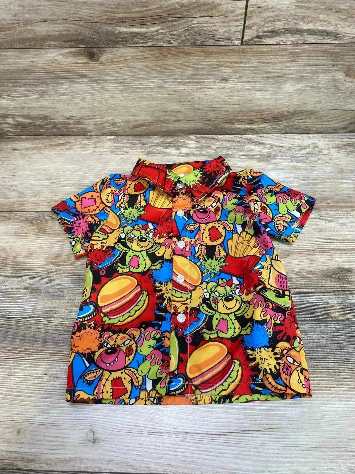 Flat-lay of children's short-sleeve button-up shirt size 4Y showcasing colorful burgers, fries, and cartoon bear print on light wood background