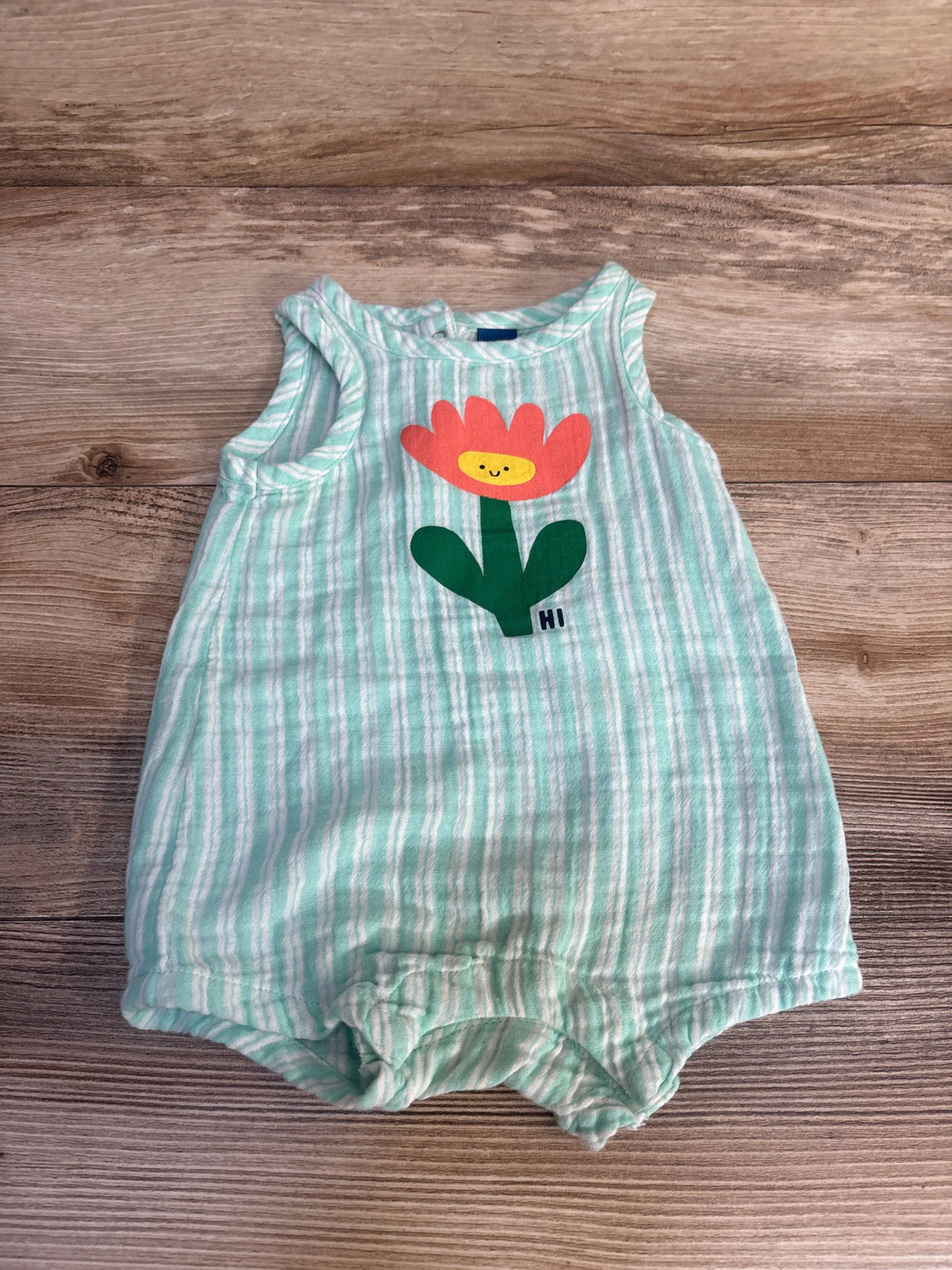 Green and white striped baby romper with a smiling flower graphic on wooden background