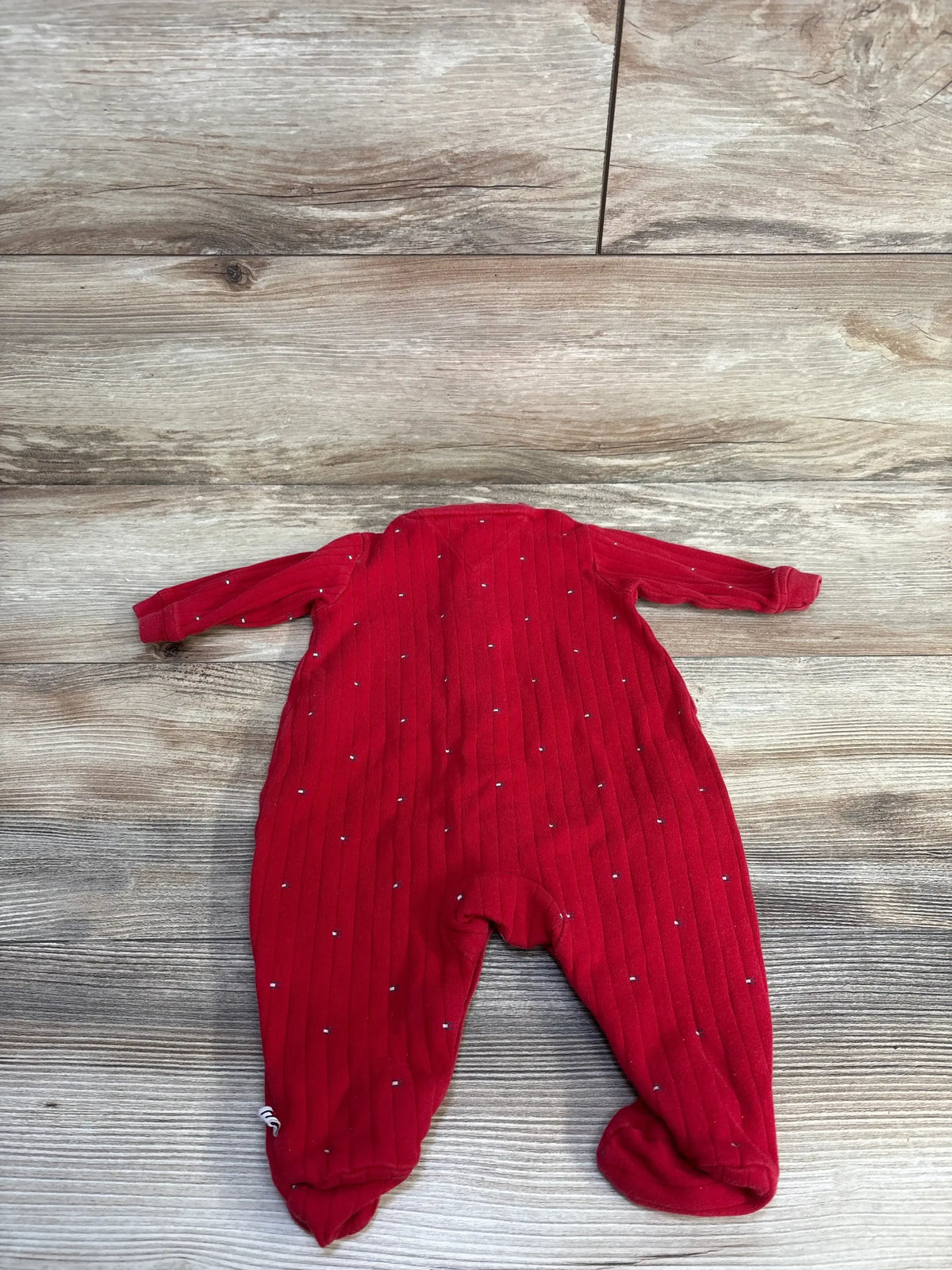 Back view of red Tommy Hilfiger newborn sleeper size 0-3M showcasing ribbed knit, small white dot pattern and footed legs on light wood floor