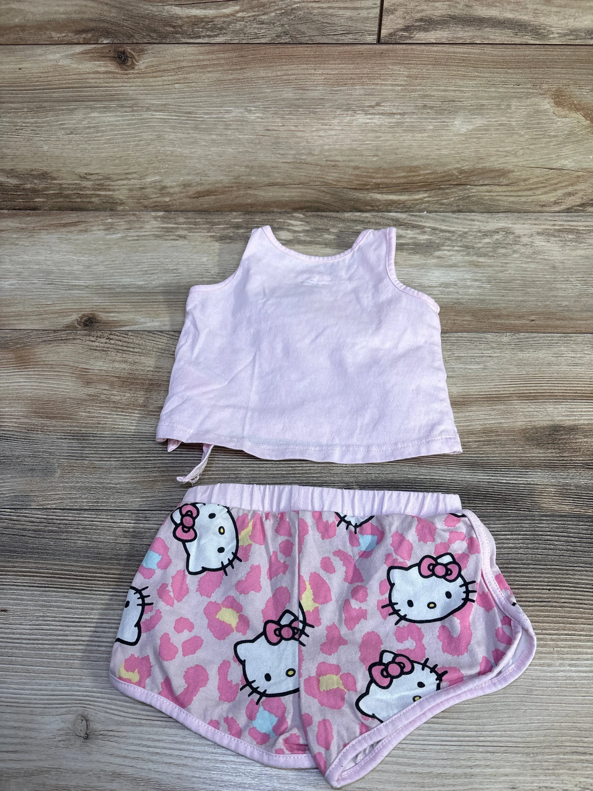 Flat lay of Hello Kitty toddler tank and shorts showing light-pink tank and pink Hello Kitty-print shorts on wood background
