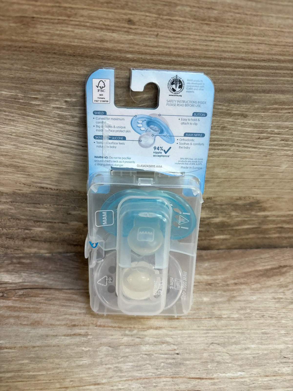 Packaged MAM baby pacifiers with blue accents on wood background, infant feeding essentials