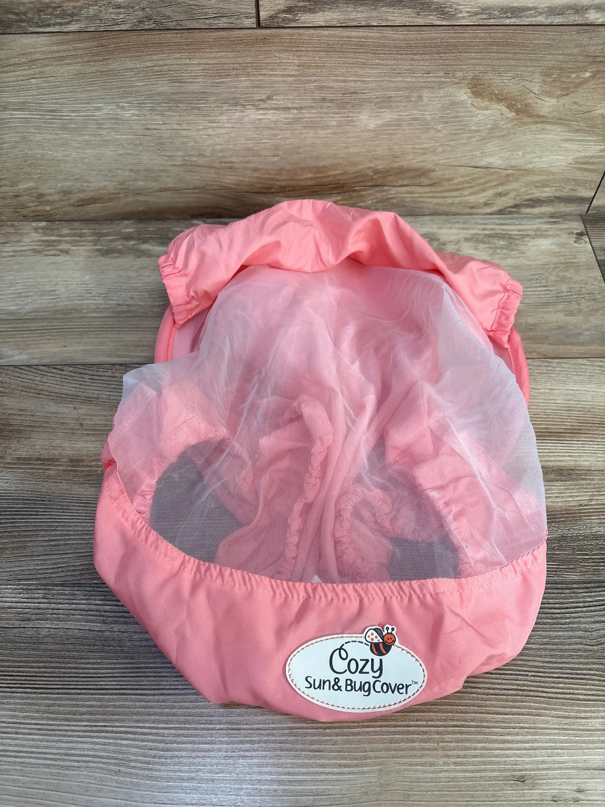 Top view of the pink Cozy Summer Sun & Bug Car Seat Cover showcasing its white mesh canopy on a wood floor