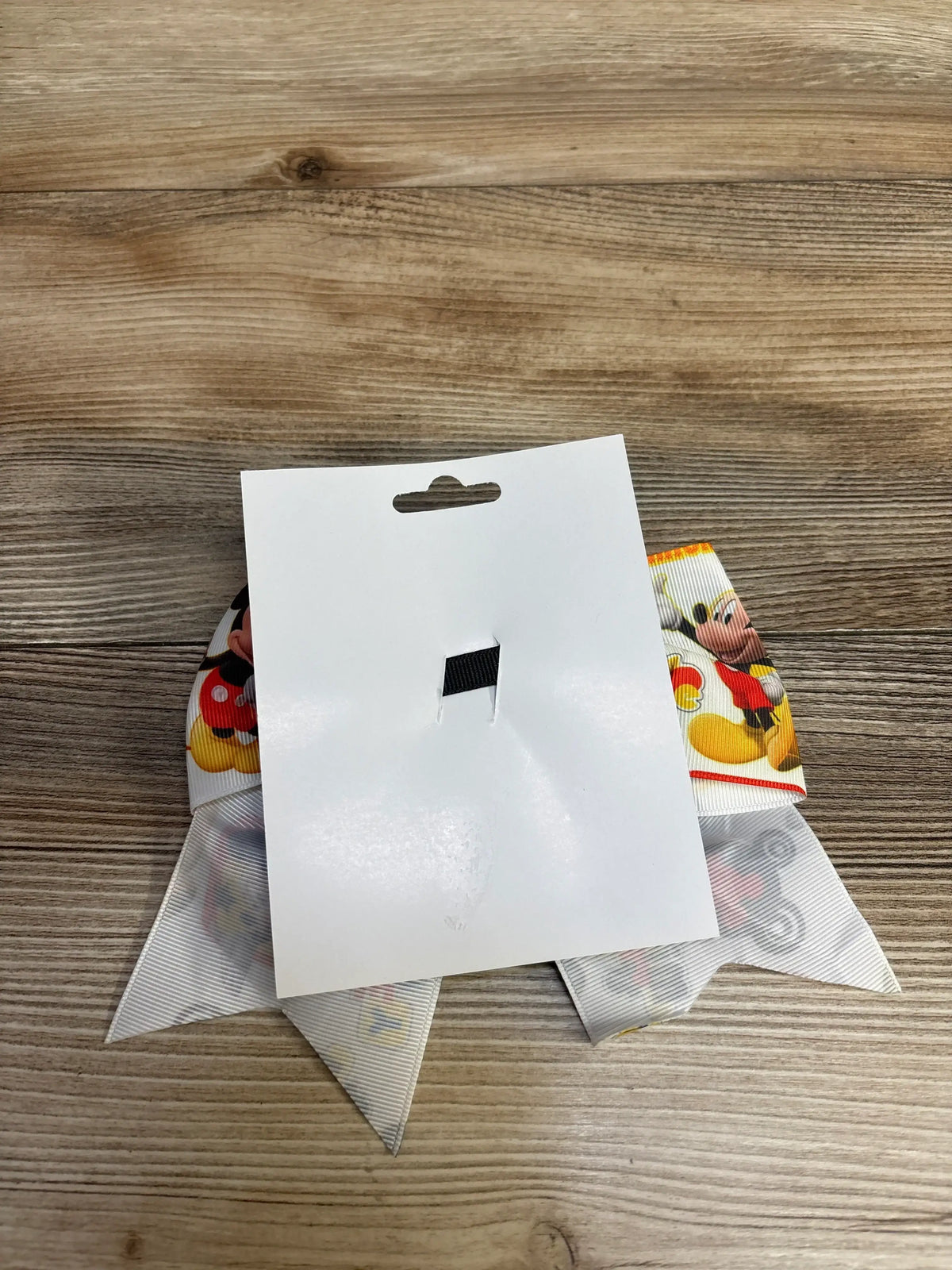 Mickey Mouse themed ribbon bow partially covered by white display card on wooden surface