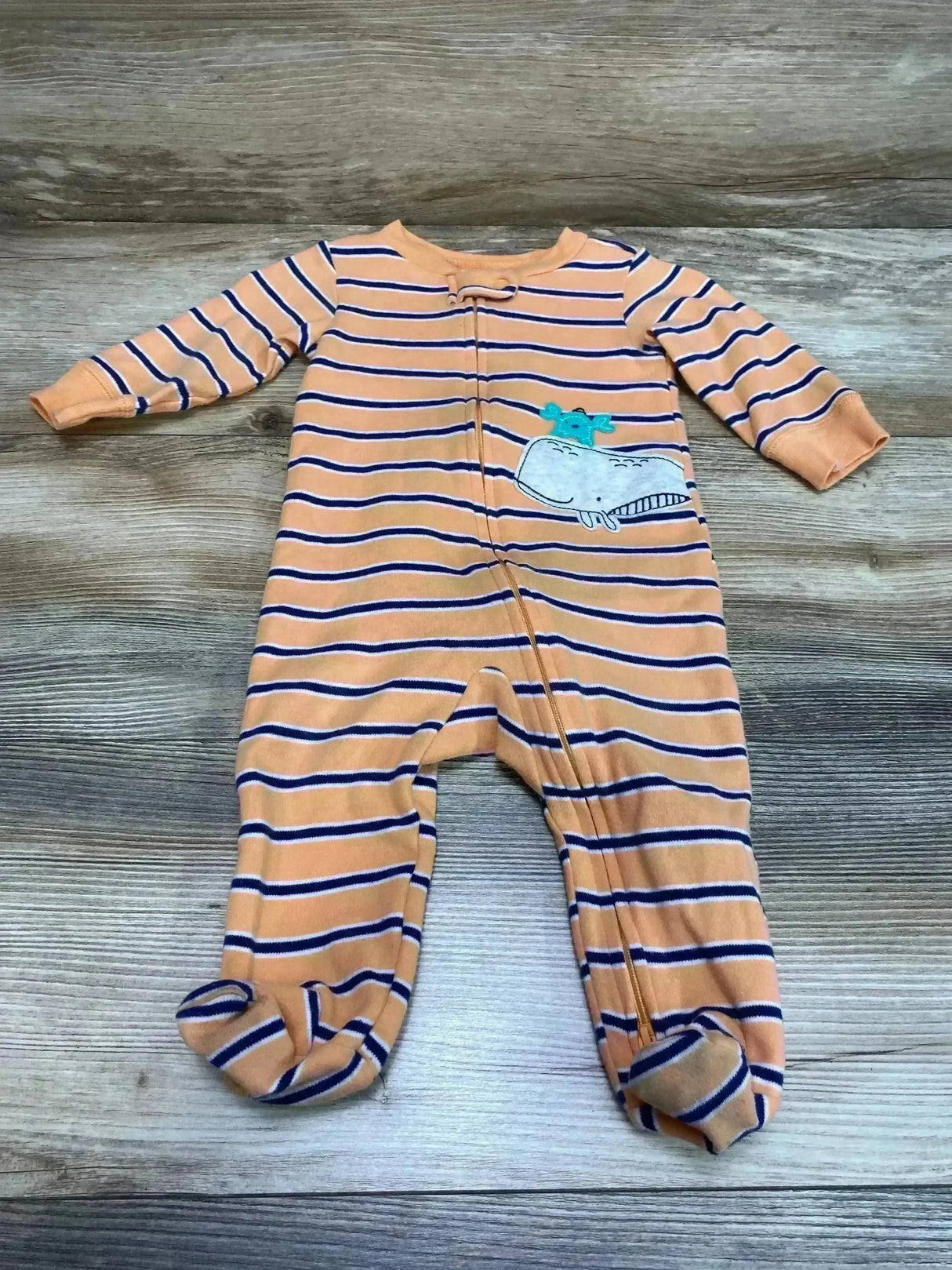 Flat-lay of Carter's orange and navy striped footed sleeper (6M) showing whale applique and front zipper on wood floor background