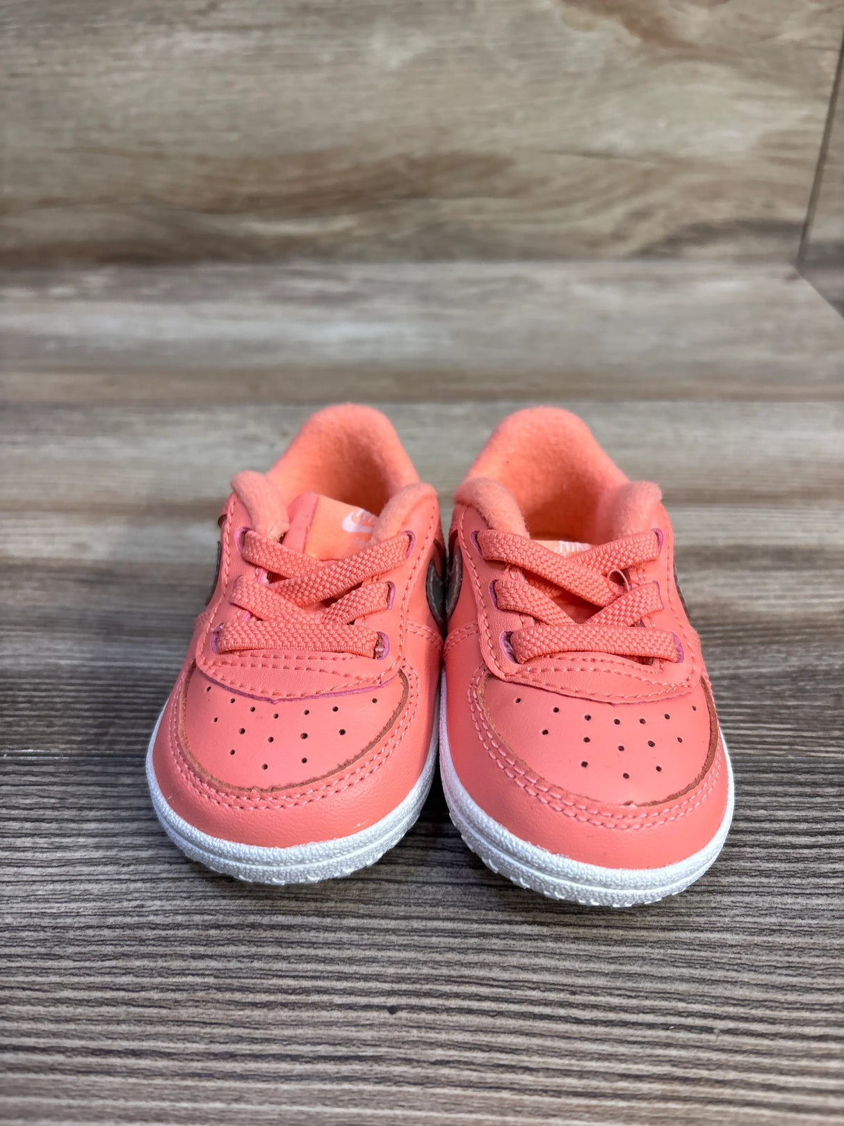 Front view of toddler Nike Force 1 CB sneakers showcasing atomic pink metallic upper and white sole on wood background