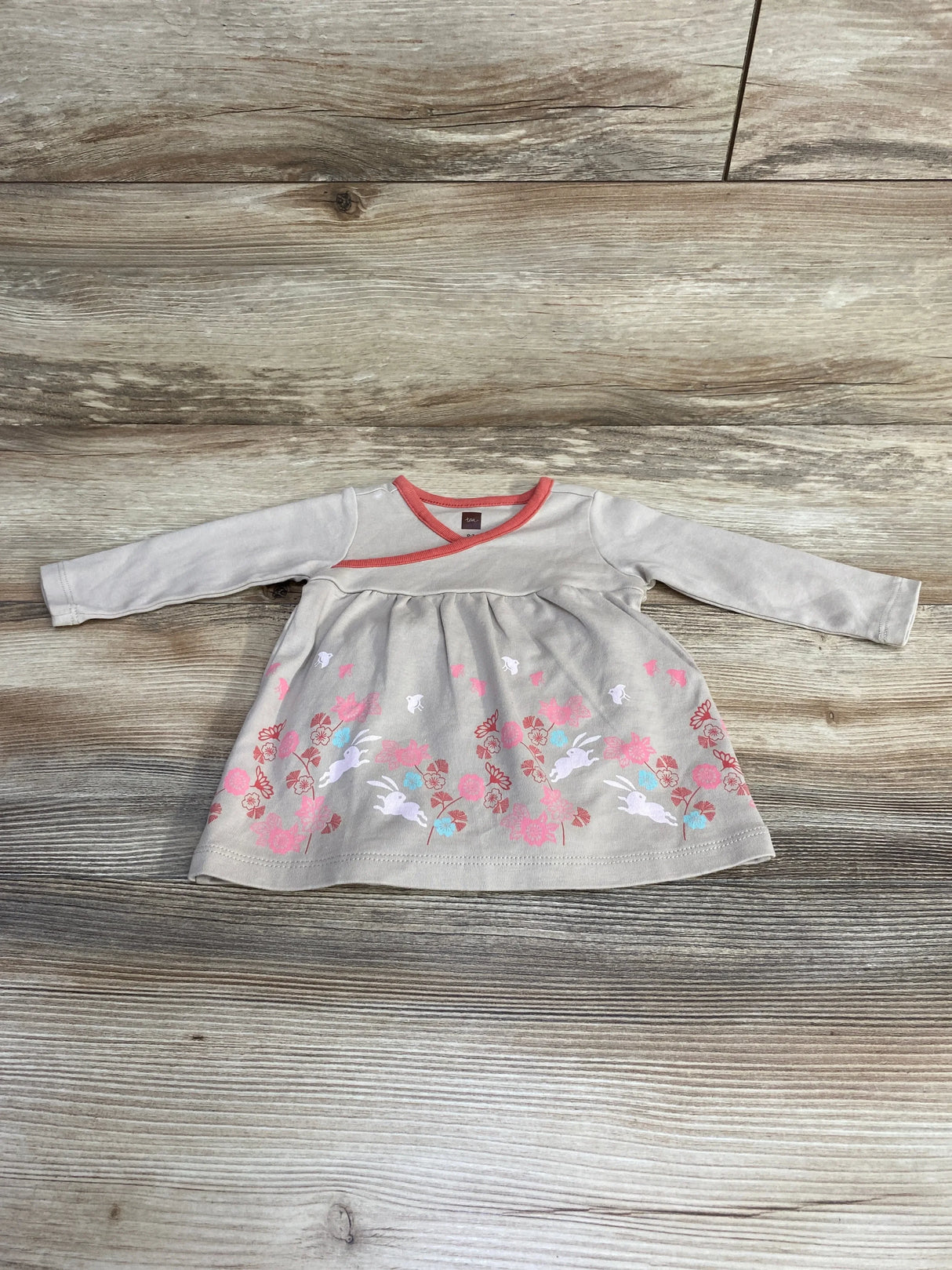 Flat lay of newborn long sleeve bunny dress showcasing pink floral and white bunny print with coral neckline on light wood