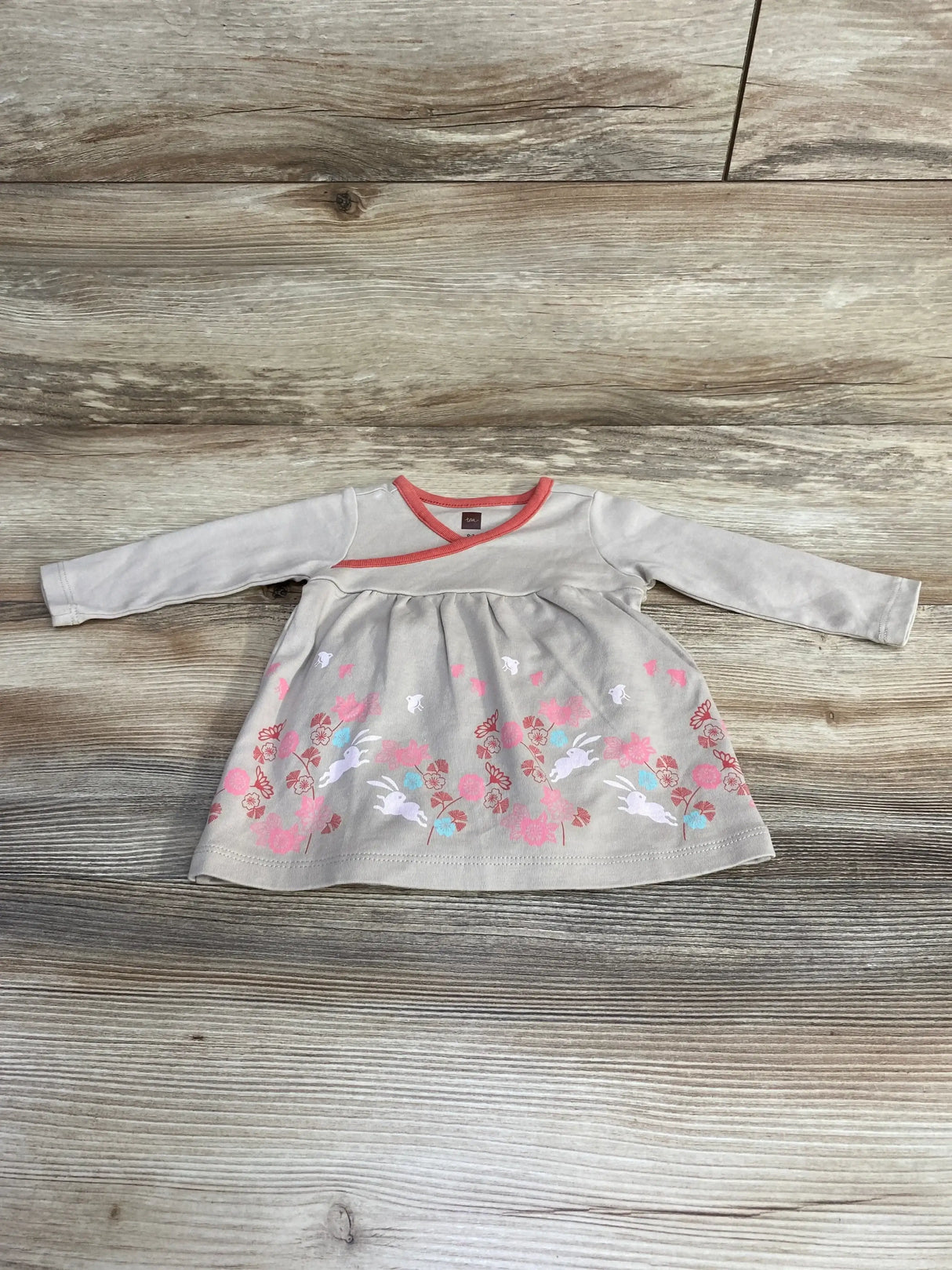 Flat lay of newborn long sleeve bunny dress showcasing pink floral and white bunny print with coral neckline on light wood