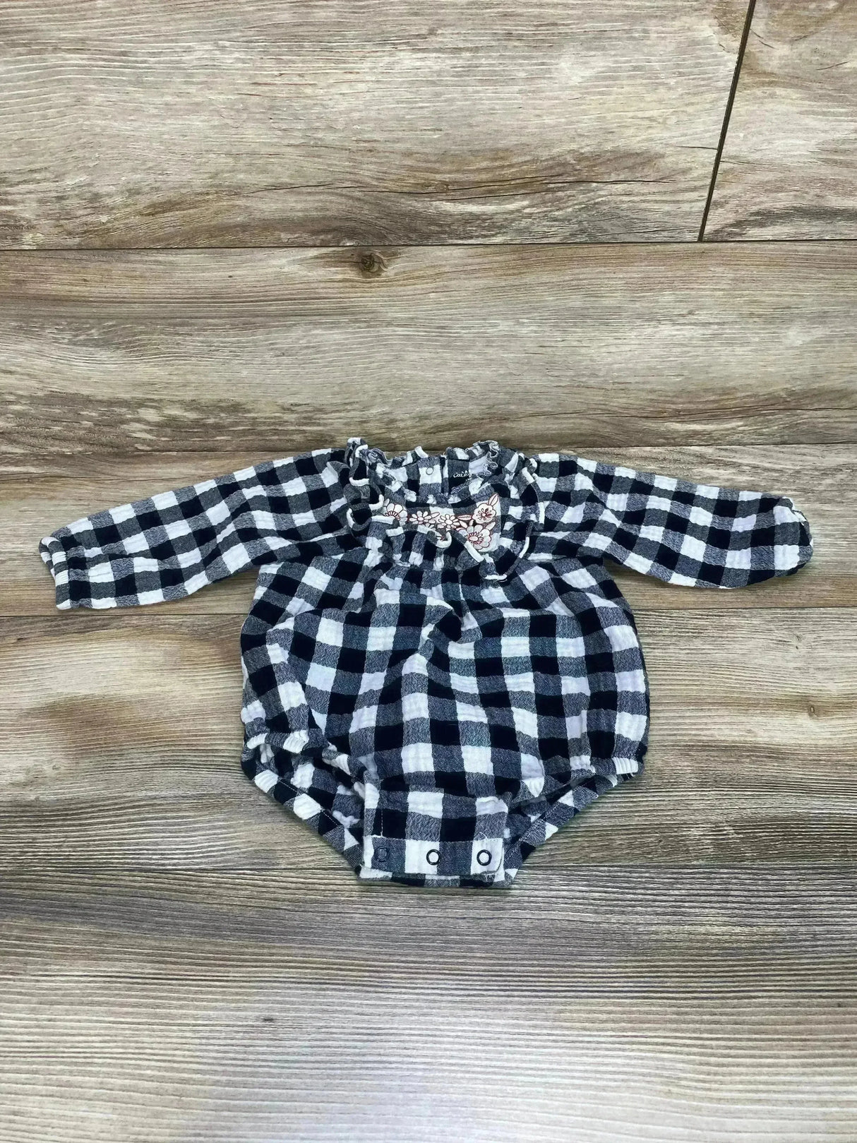 Flat lay of Cat & Jack baby bubble romper in black and white buffalo check with ruffled embroidered collar, long sleeves, and snap crotch on wood background