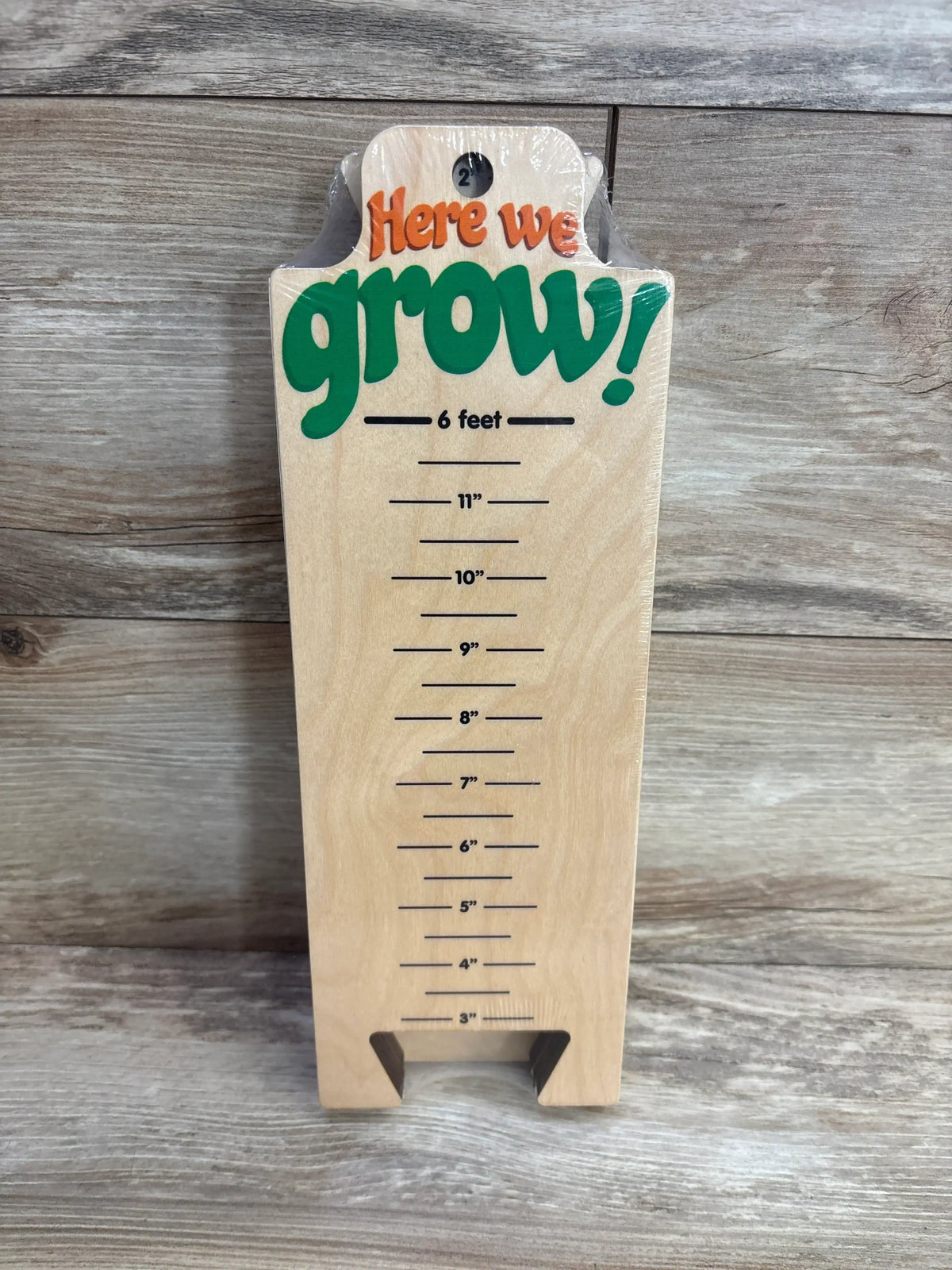 Wooden kids growth chart ruler with colorful 'Here we grow!' text for tracking height.