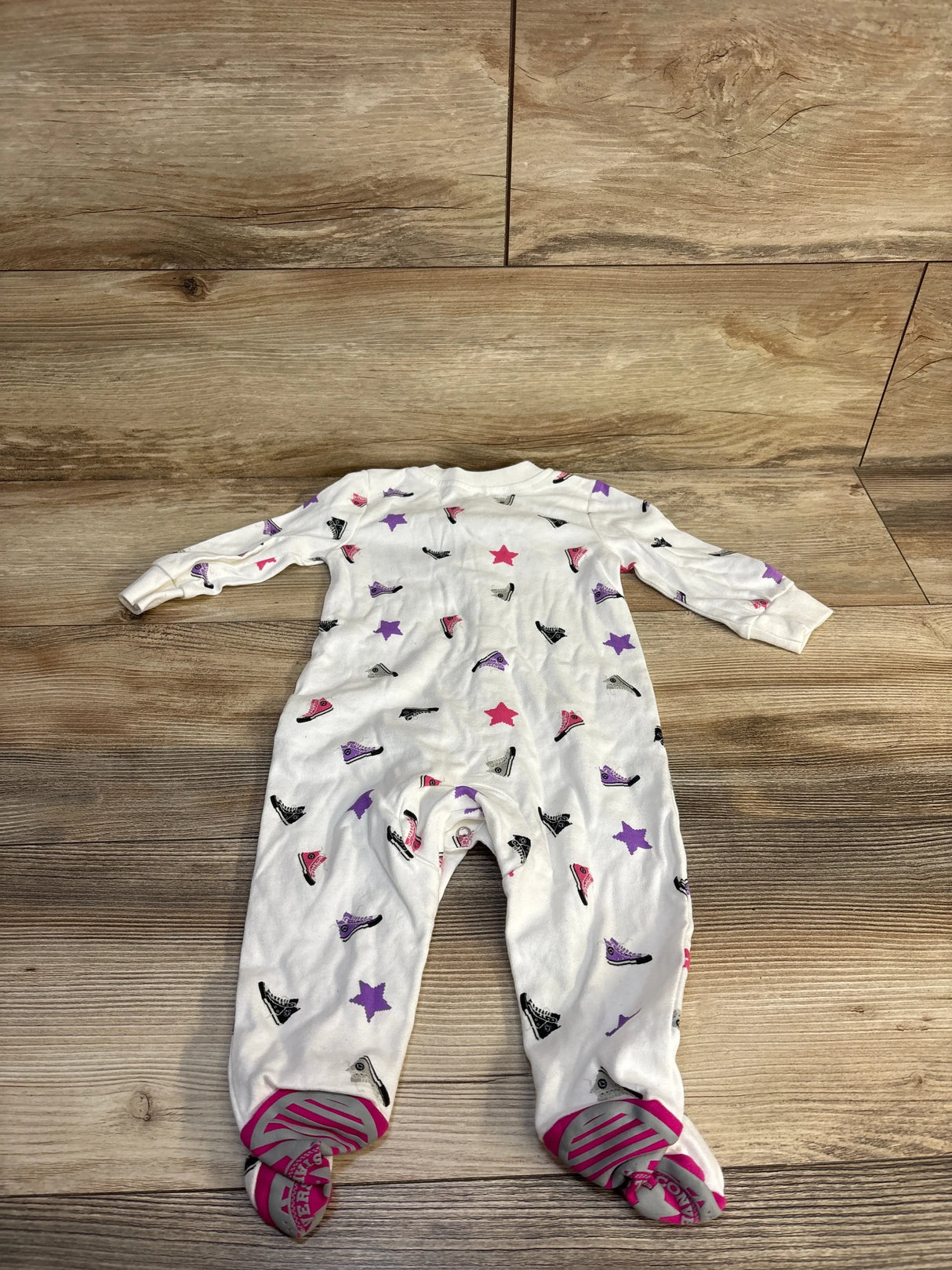 White baby onesie with colorful sneaker and star print, footed design on wood floor
