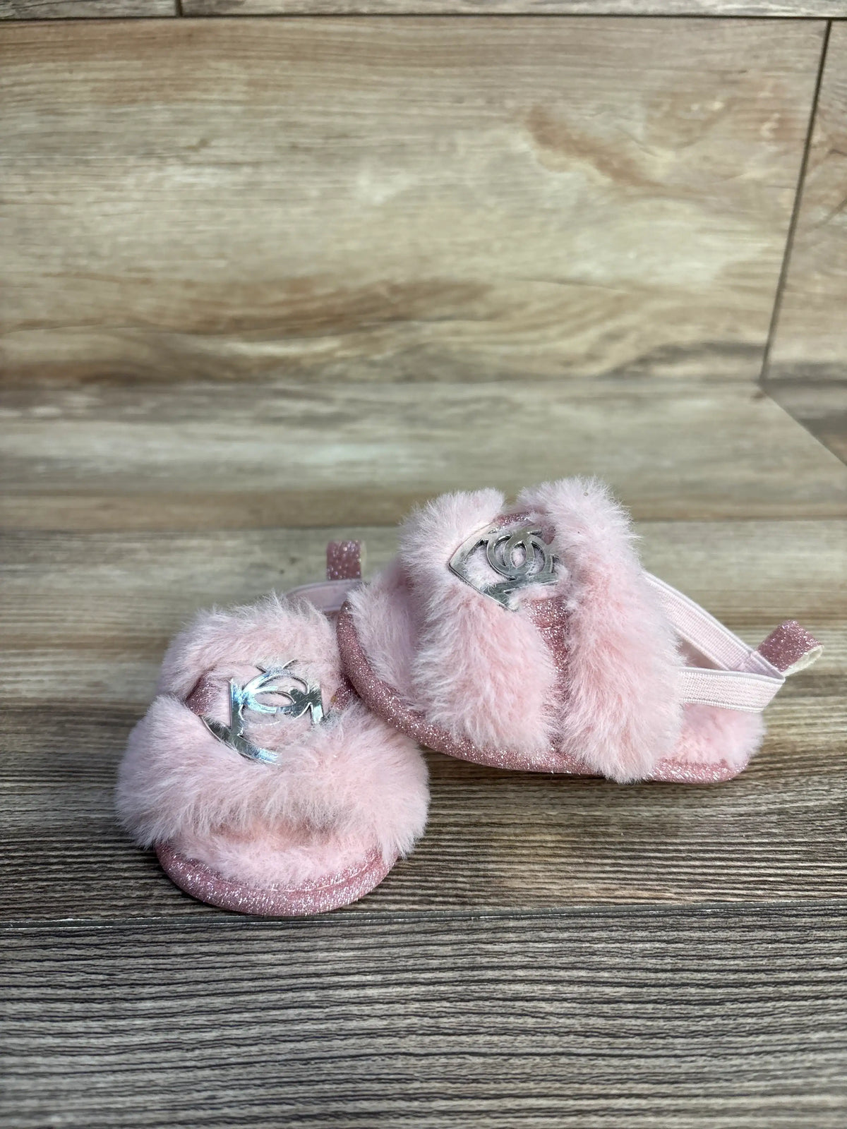 Pair of pink faux fur slide sandals with silver embellishments on a wooden background