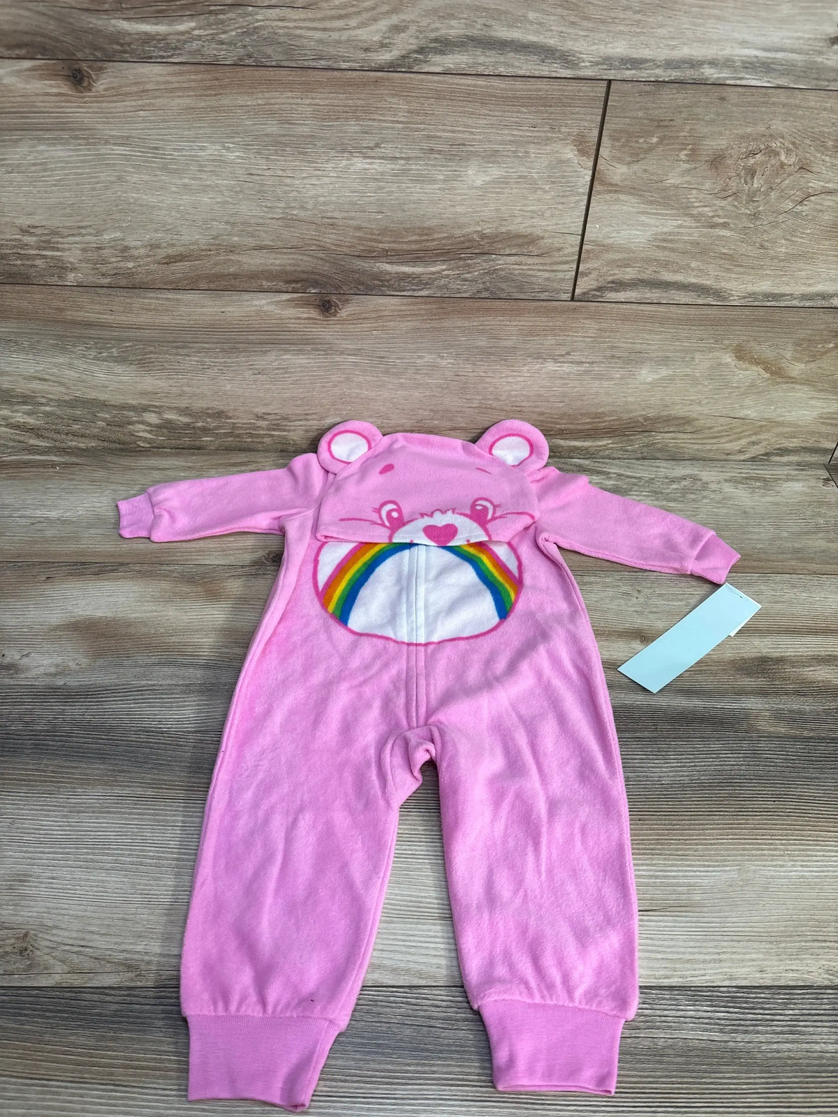 Flat lay of pink Care Bears 2-piece sleeper and hat set 12M showing bear hood with ears and rainbow belly on wood floor