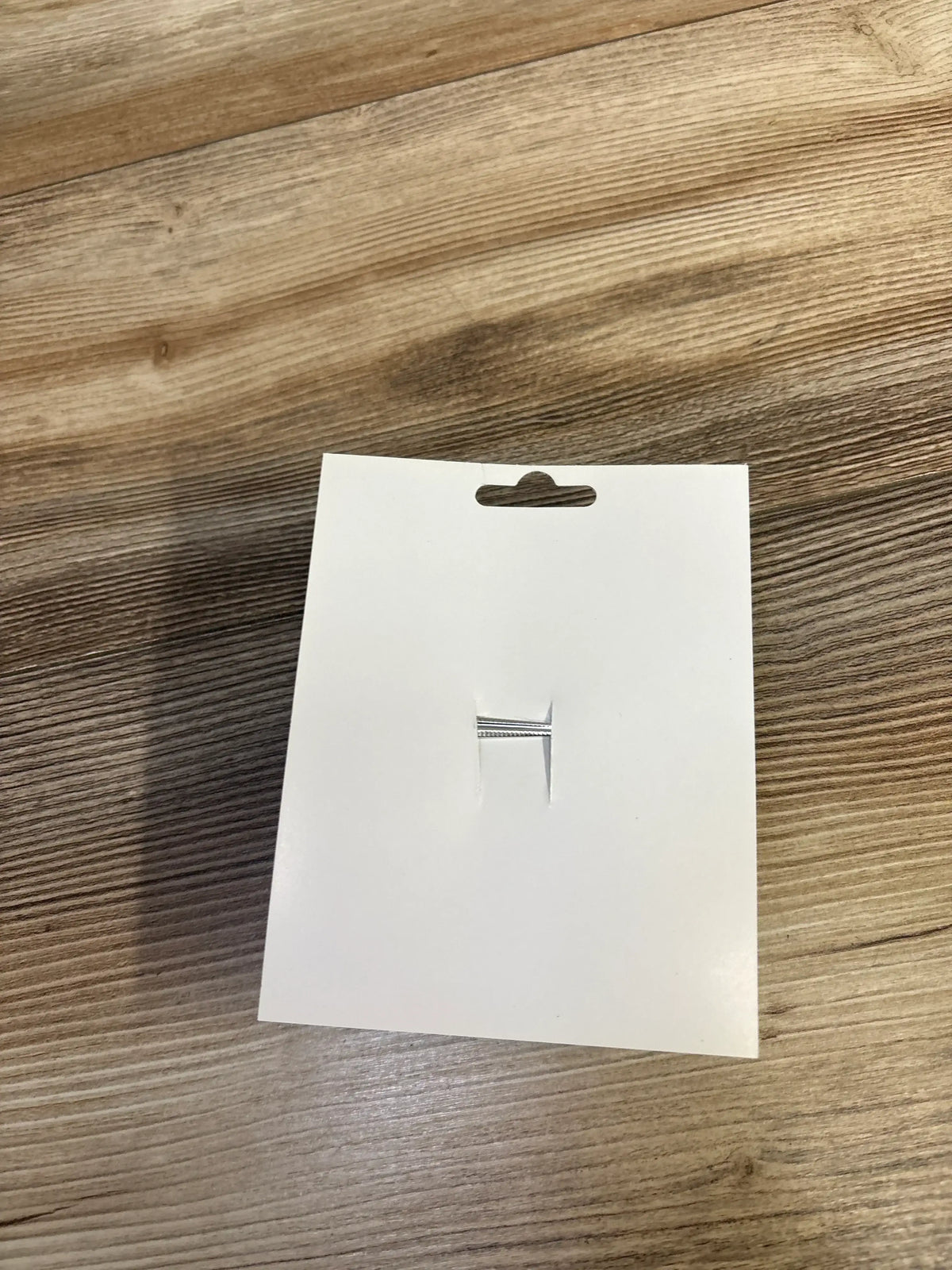 White jewelry display card with a silver bracelet on a wood surface